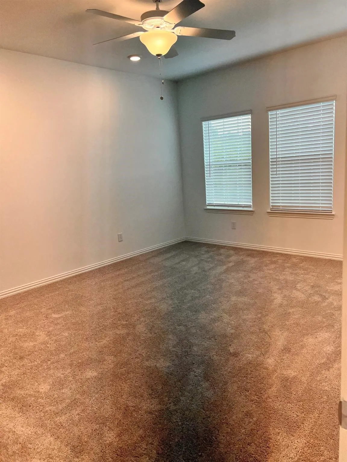 Spacious room featuring neutral carpeting, a ceiling fan with integrated lighting, recessed lighting, and two windows with blinds