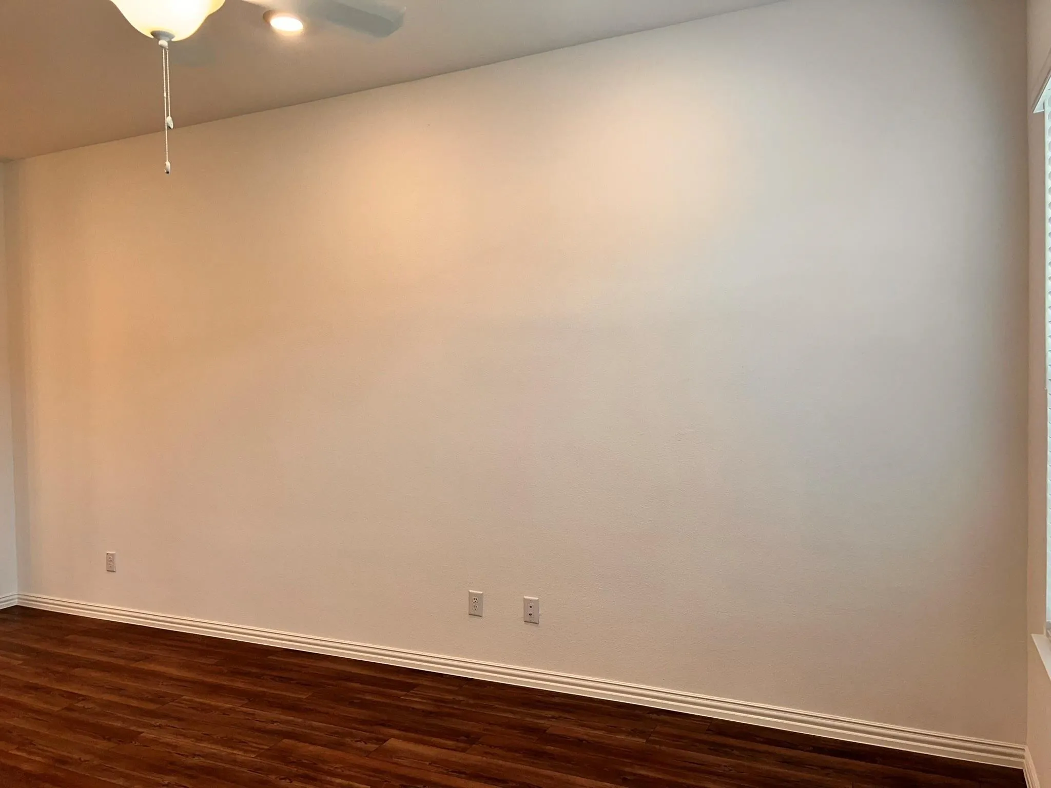 Spacious room featuring wood-finish flooring, white baseboards, and a ceiling fan with integrated lighting