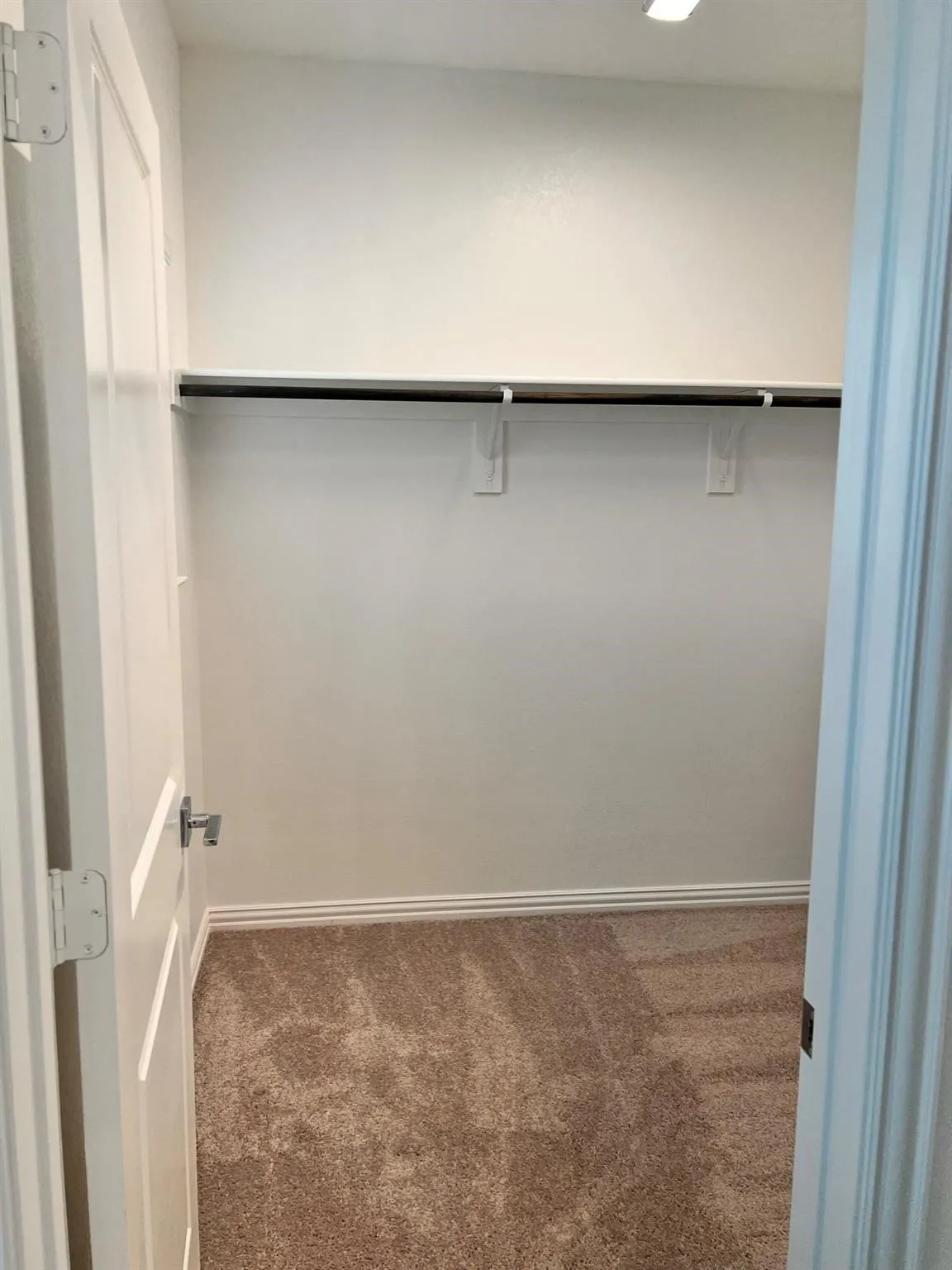 Carpeted closet with white walls and a single hanging rod