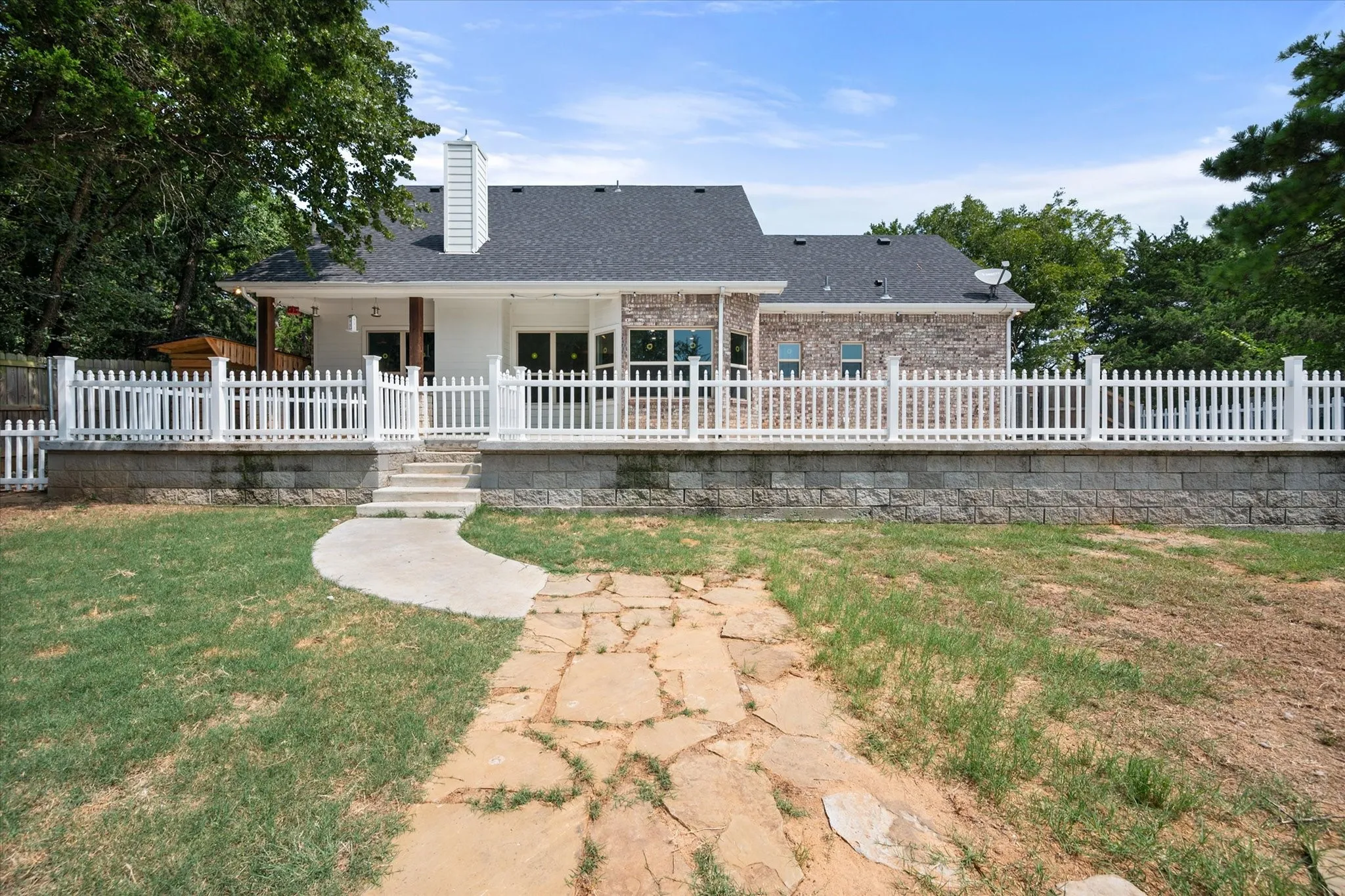 Rear exterior featuring a dark gray shingle roof and a combination of white siding and brick masonry.
