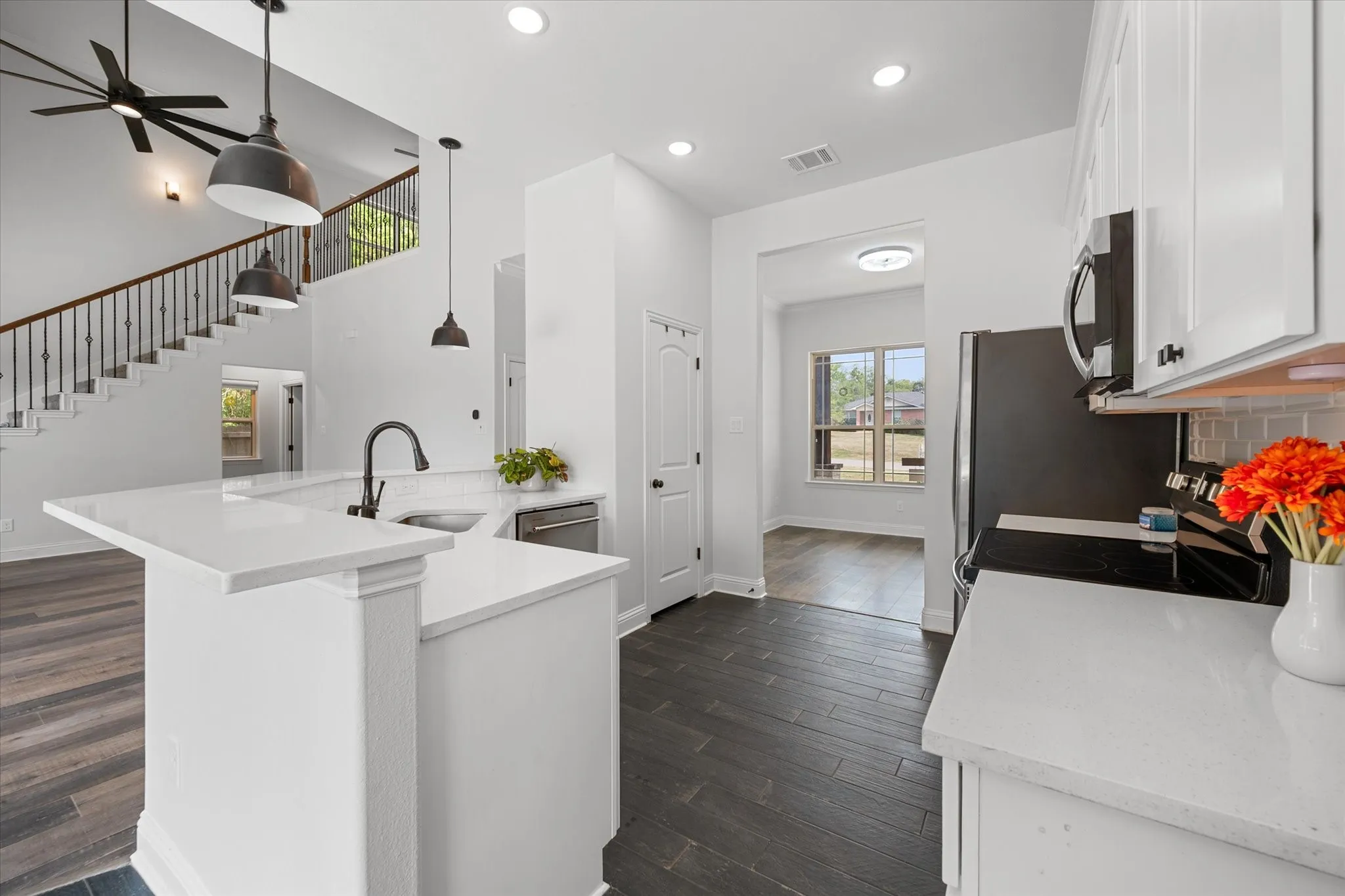 Kitchen is open to the living area and features a pantry, white cabinetry, light quartz countertops, subway tile backsplash, and dark tile flooring