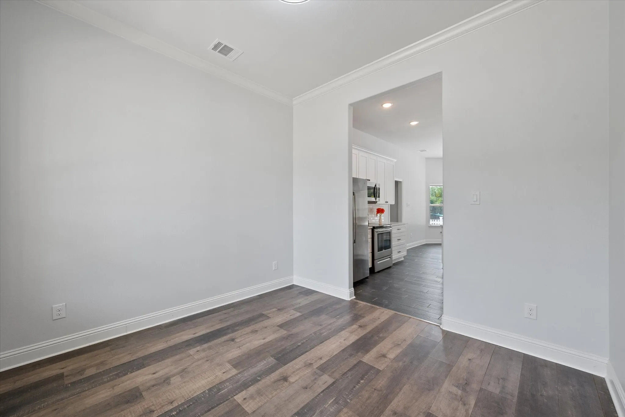 Dining room featuring wood-finish flooring, light gray walls, crown molding, white baseboards and access to the kitchen.