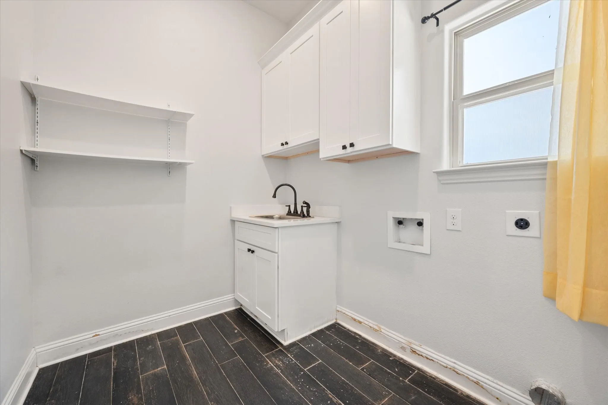 Oversized laundry room is located downstairs and features white cabinetry with dark hardware, a utility sink with a matte black faucet, and a window looking out to the backyard