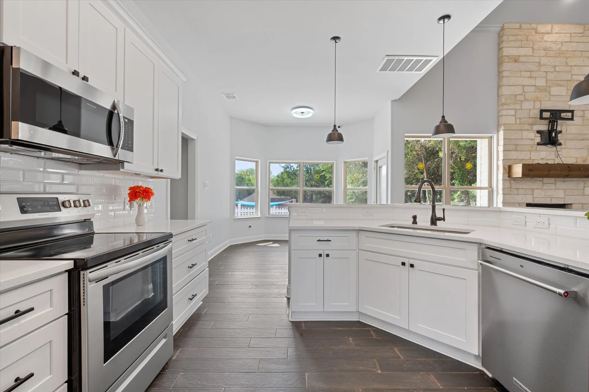 Sophisticated kitchen featuring white shaker cabinetry with black hardware, stainless steel appliances including a microwave and dishwasher, white subway tile backsplash, and dark wood-finish flooring