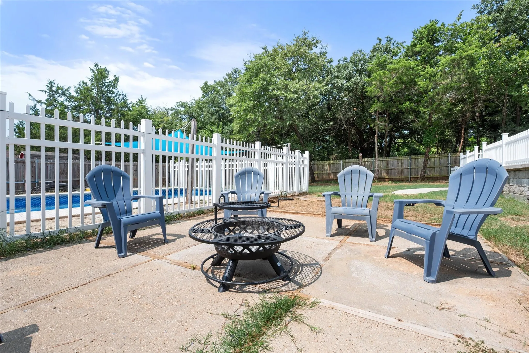 Patio area featuring a fire pit, concrete pavers, and a white picket fence enclosing a swimming pool