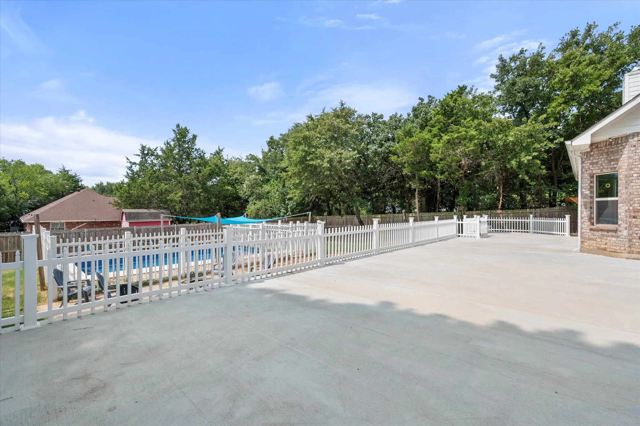 Expansive concrete patio bordered by a white picket fence overlooks the backyard and inground swimming pool
