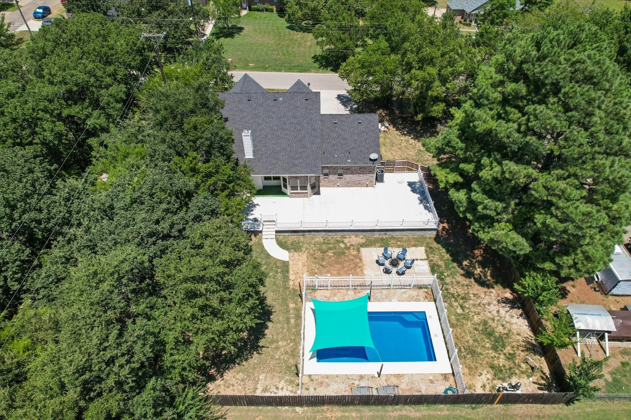 Expansive backyard featuring a fenced-in swimming pool with a shade sail, a fire pit area, and a large elevated concrete deck