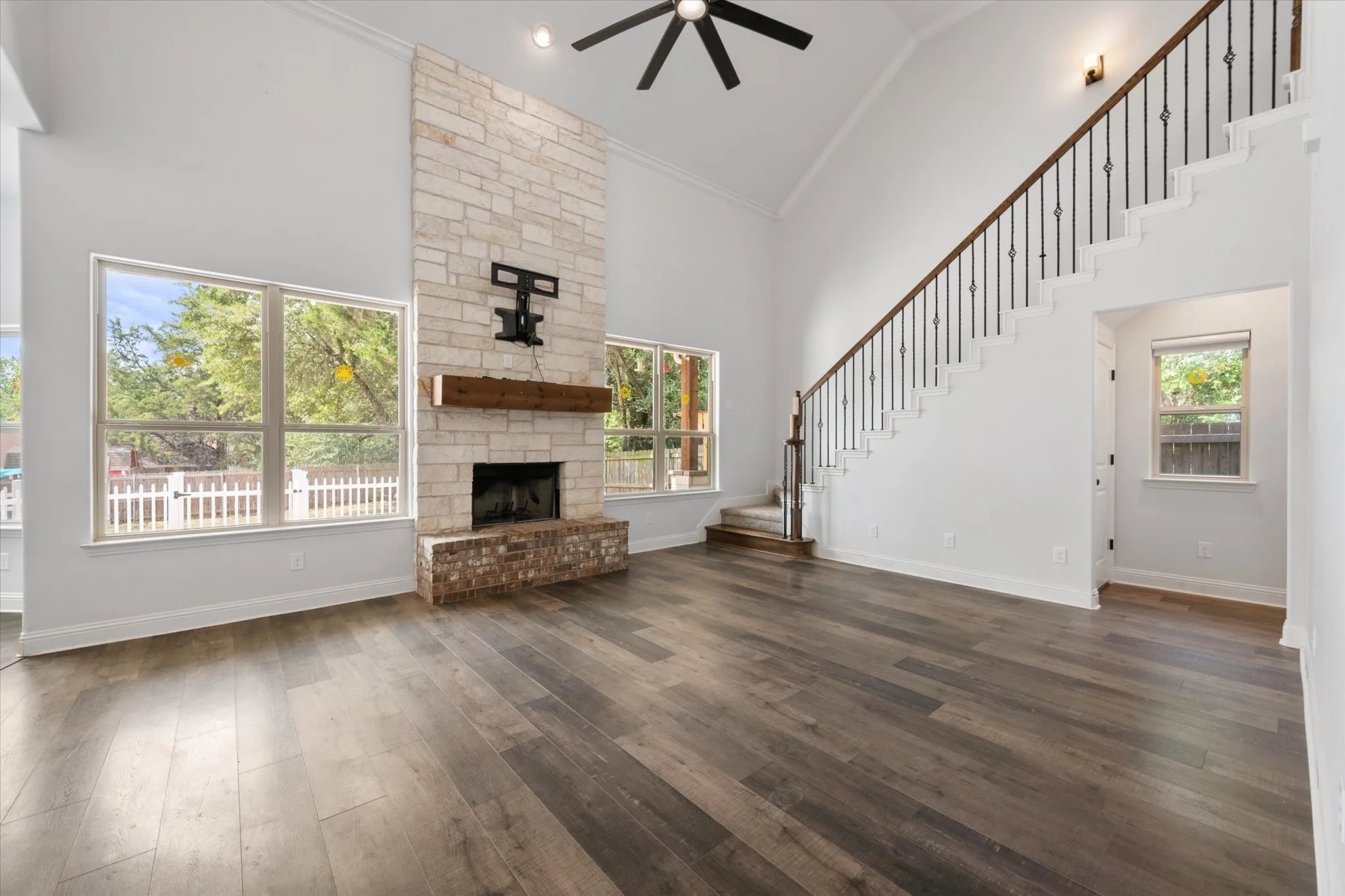 Soaring two-story great room showcasing a stone fireplace with wood mantel and abundant natural light from expansive windows