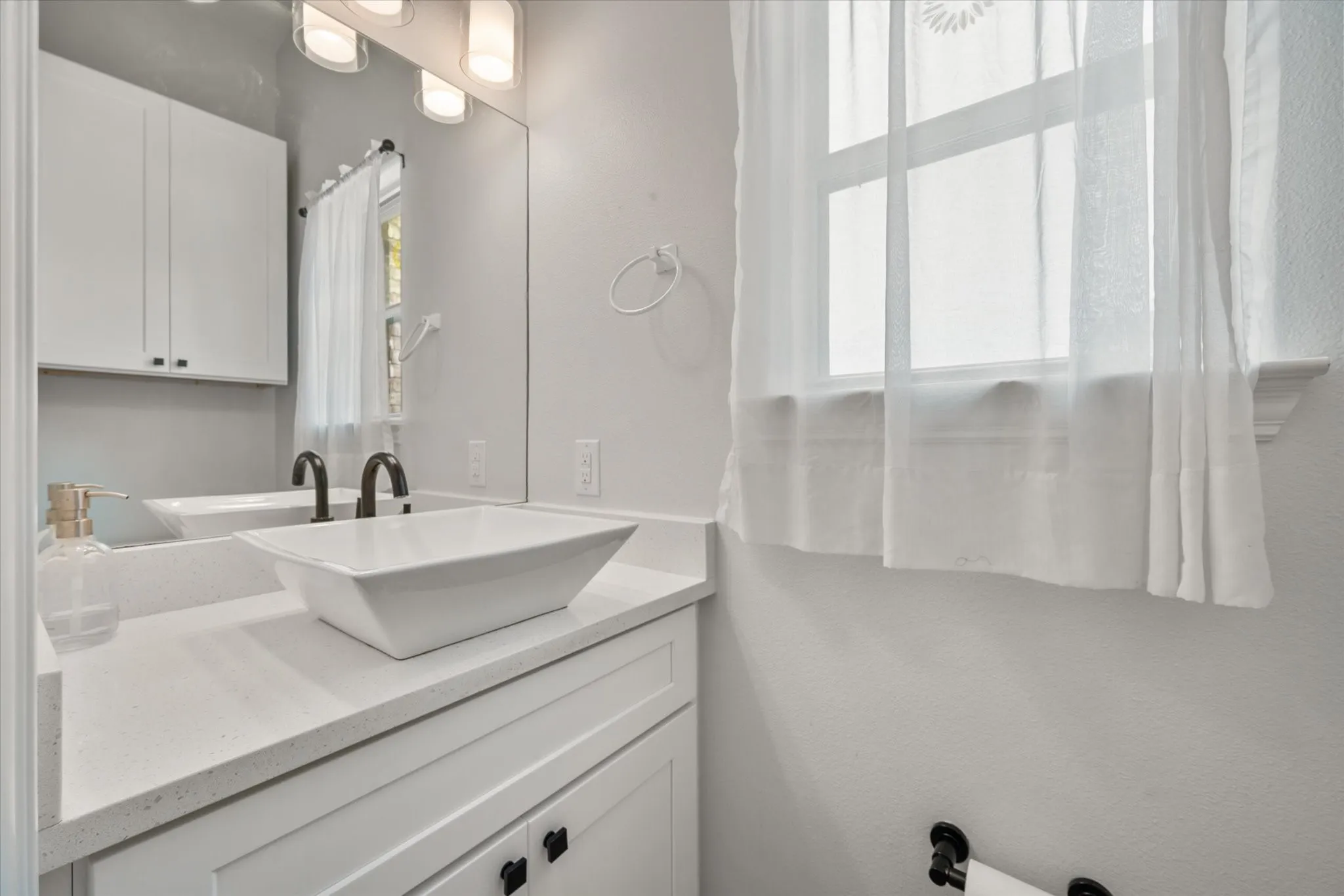 There is a half bathroom located conveniently downstairs for guests featuring a rectangular vessel sink and quartz countertop - window also views the backyard.