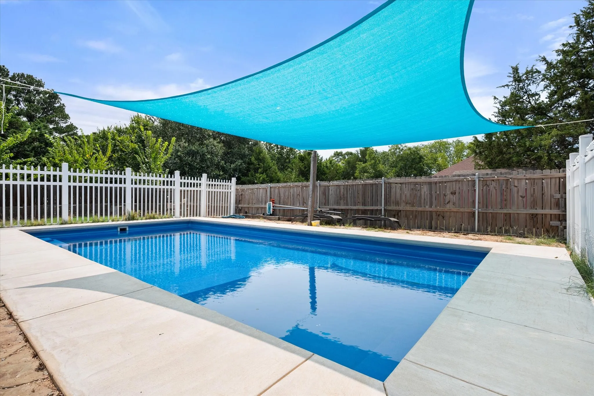 Rectangular swimming pool featuring a concrete surround and an overhead shade sail