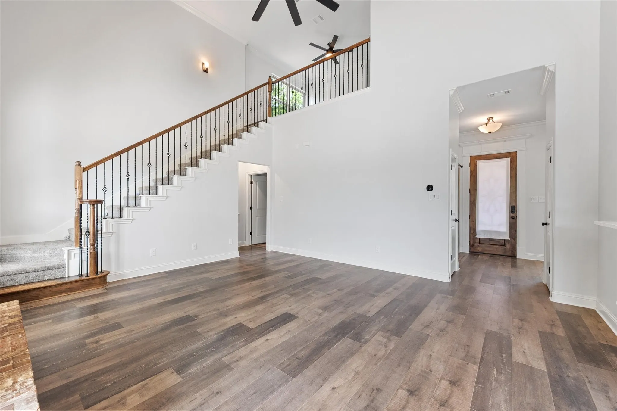 Another view of the living area looking back towards the front entry on the left and the doorway on the left leads to the private primary suite.   Prominent staircase with dark metal balusters and wood handrails leads to the upstairs 2nd living area