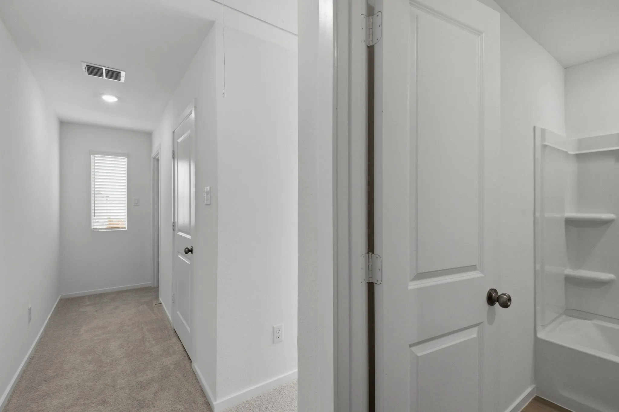 Carpeted hallway with a window featuring horizontal blinds