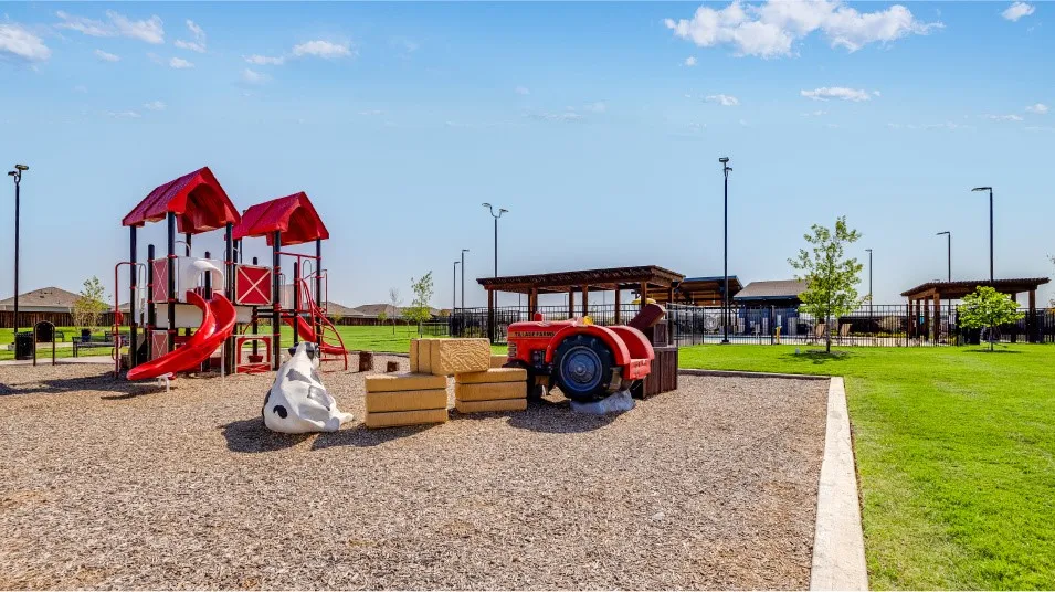 Community playground featuring a multi-level play structure with red slides, a tractor-themed play element, and a cow-shaped spring rider