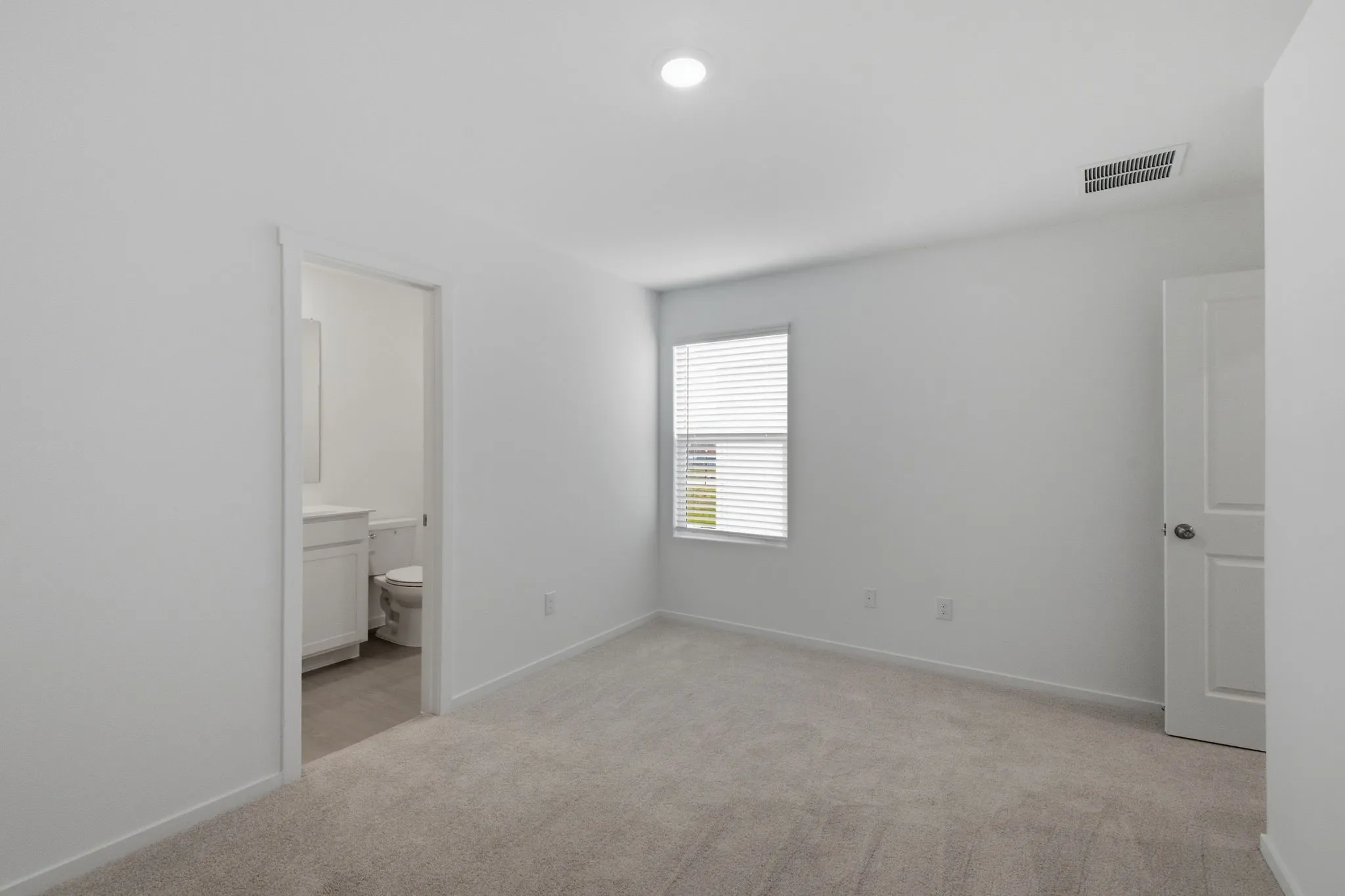 Spacious room featuring neutral carpet flooring, white walls, a single window with blinds, and a flush-mount ceiling light