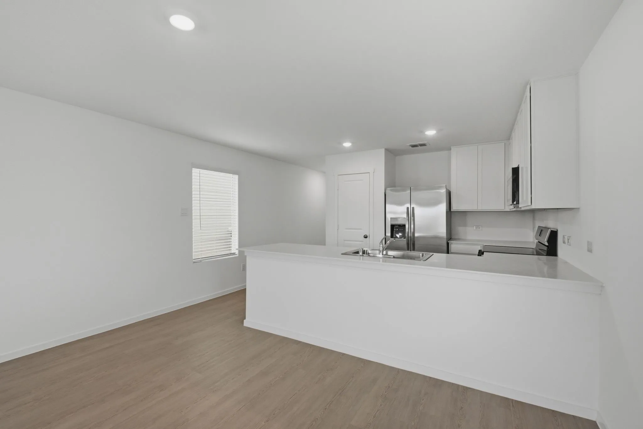 Open-concept living space featuring wood-finish flooring, recessed lighting, and a kitchen with stainless steel appliances, white cabinetry, and a peninsula with a sink