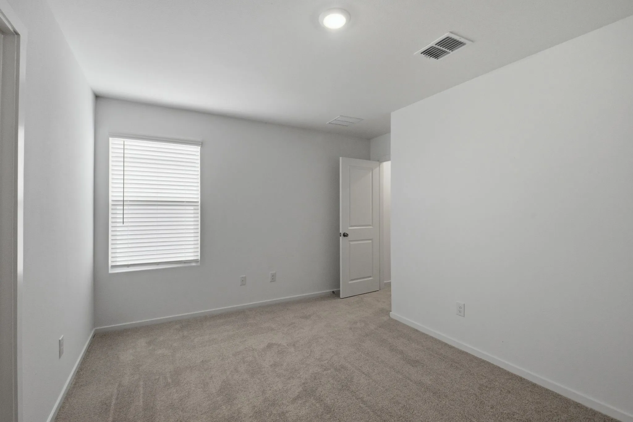 Carpeted room featuring a single window with blinds, white walls, and a recessed ceiling light