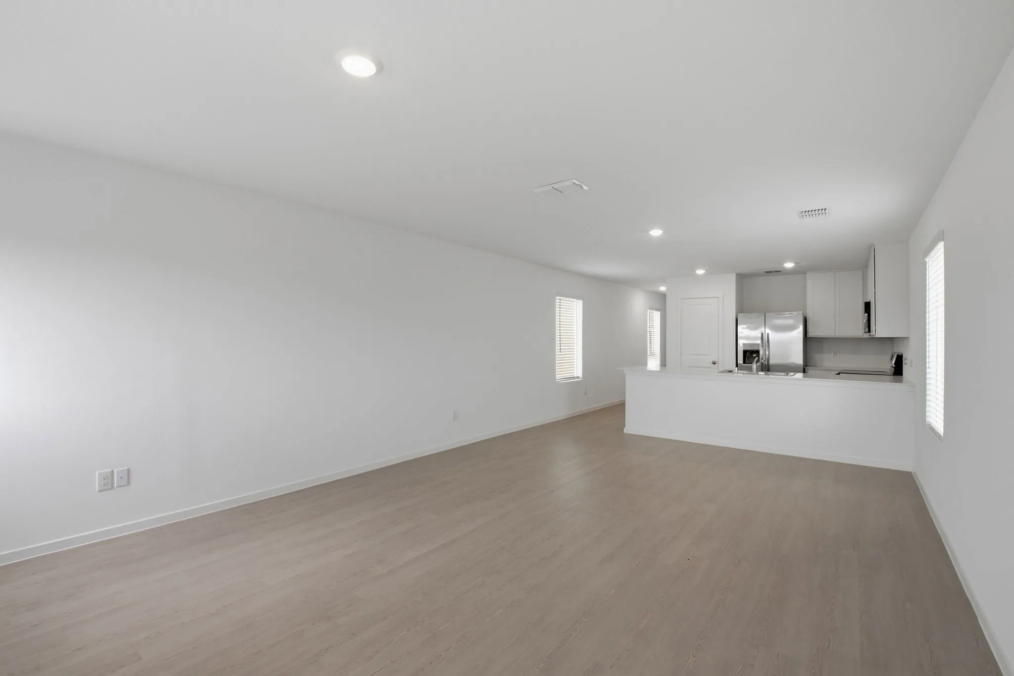 Open-concept living space with light wood-finish flooring, recessed lighting, and crisp white walls