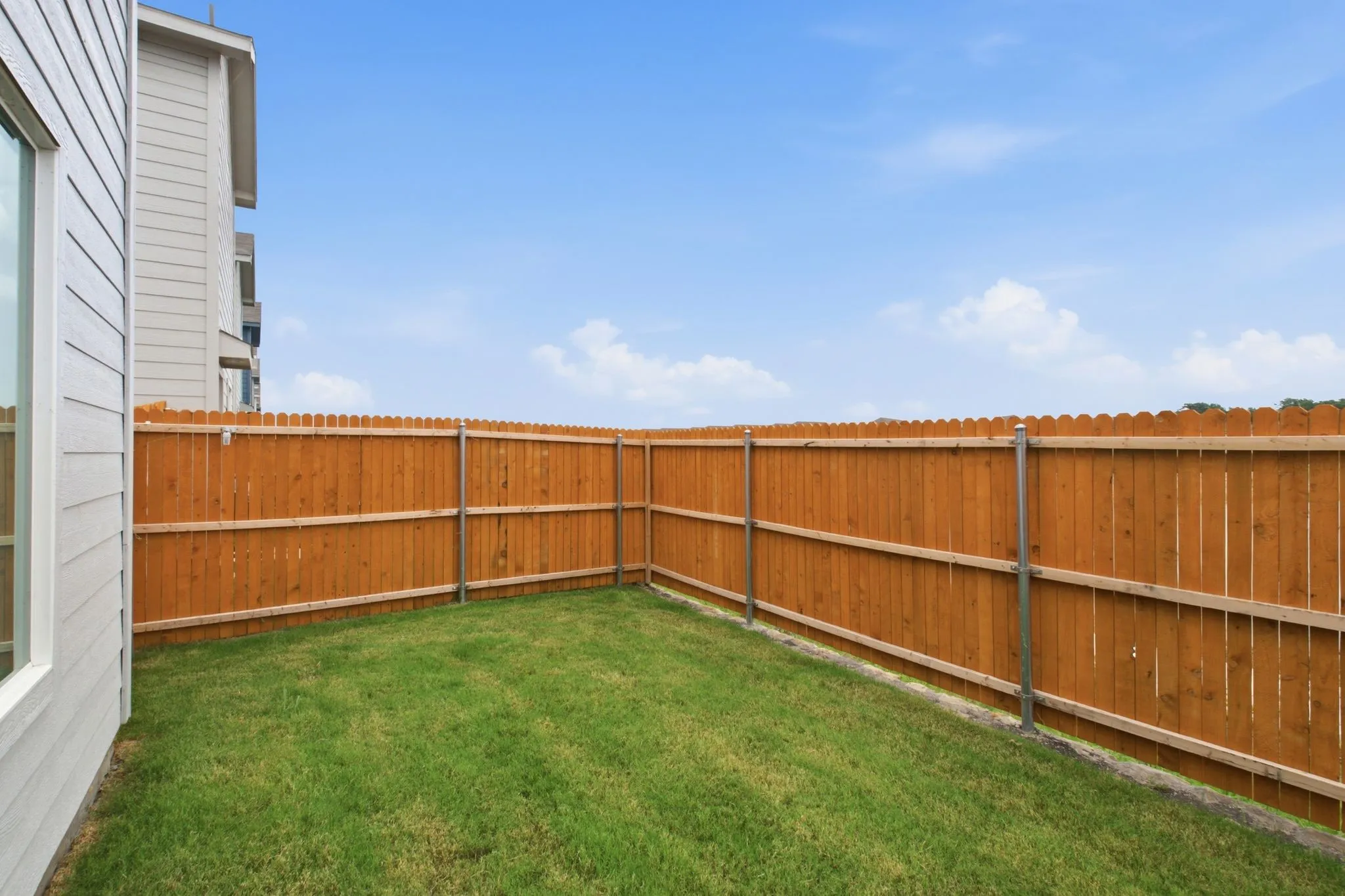 Private backyard space featuring a wood privacy fence, green lawn, and a light-colored exterior wall with a window