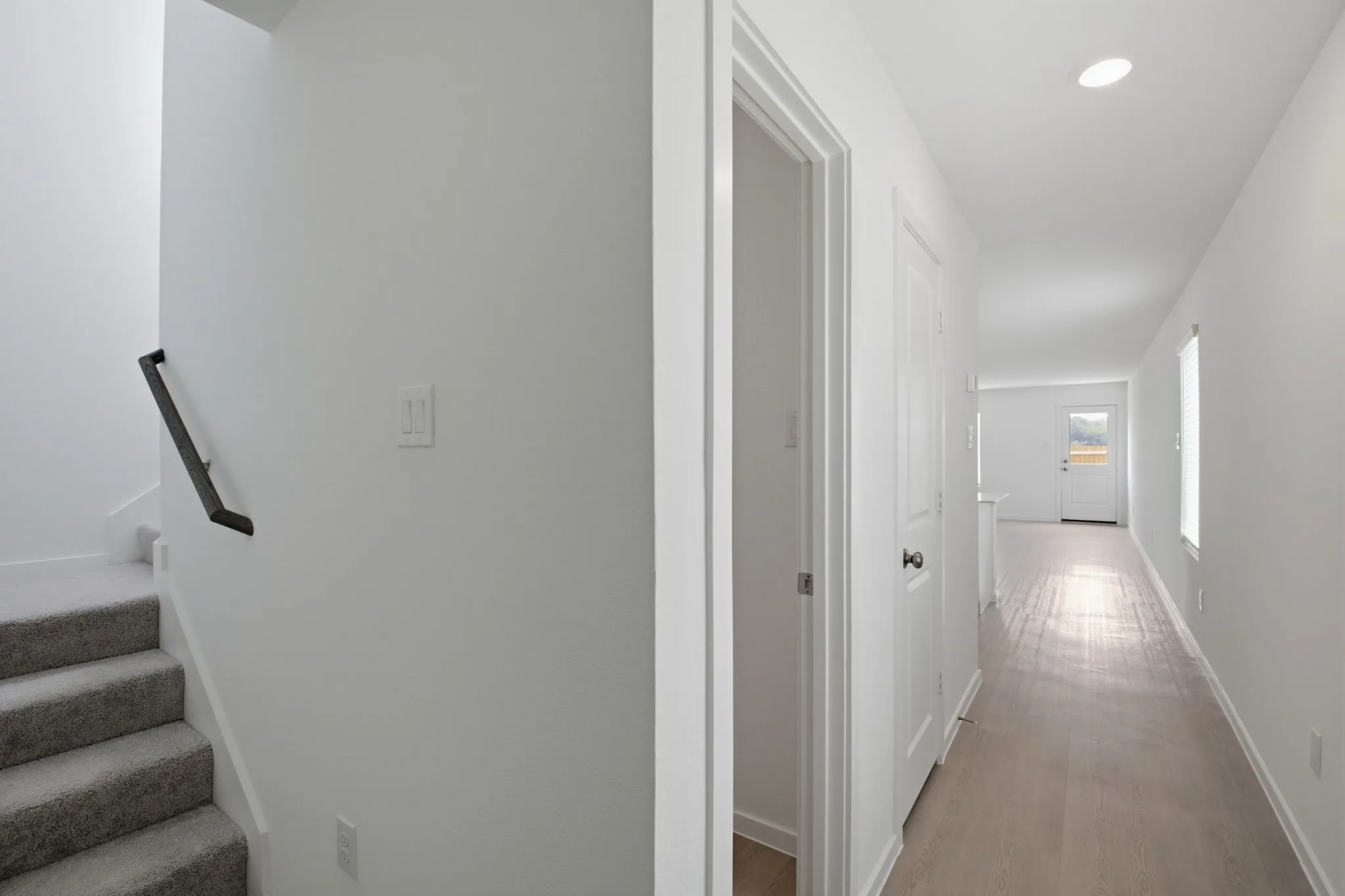 Bright hallway featuring light wood-finish flooring, recessed lighting, and white walls