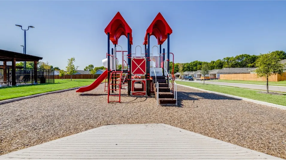Outdoor play structure with red slides and blue support beams, set on a wood chip surface