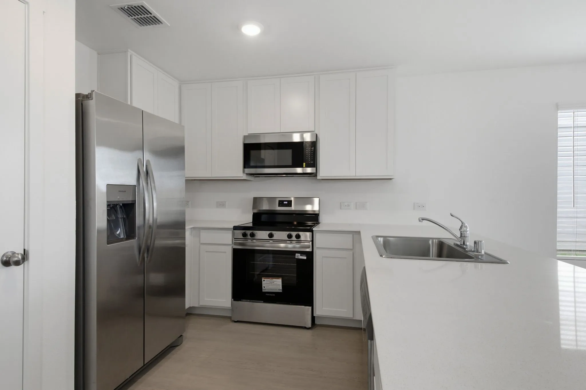 Modern kitchen featuring stainless steel appliances, white cabinetry, a spacious white countertop, an integrated sink, and wood-finish flooring