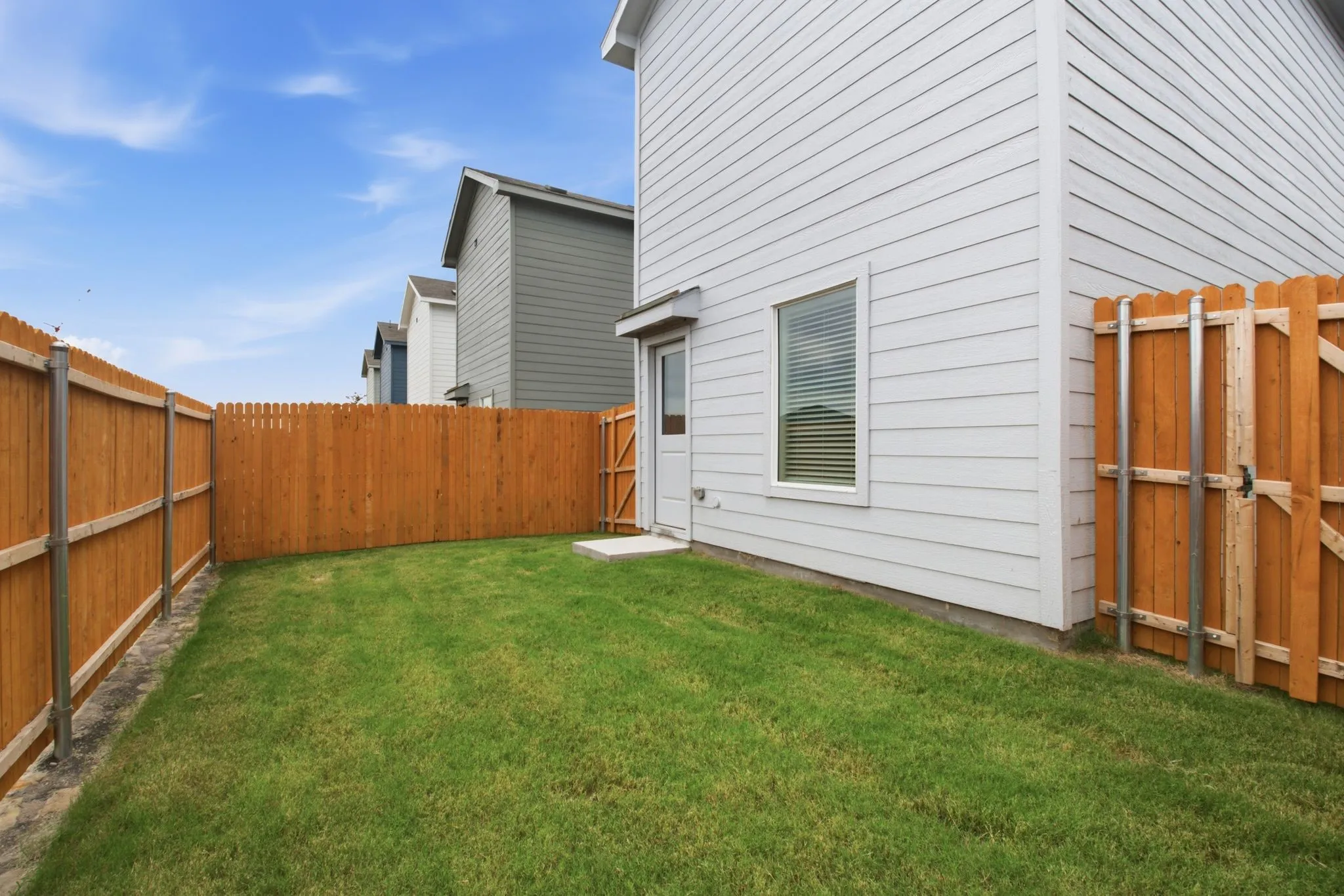 Private backyard featuring a manicured lawn, wood privacy fencing, and a side access gate