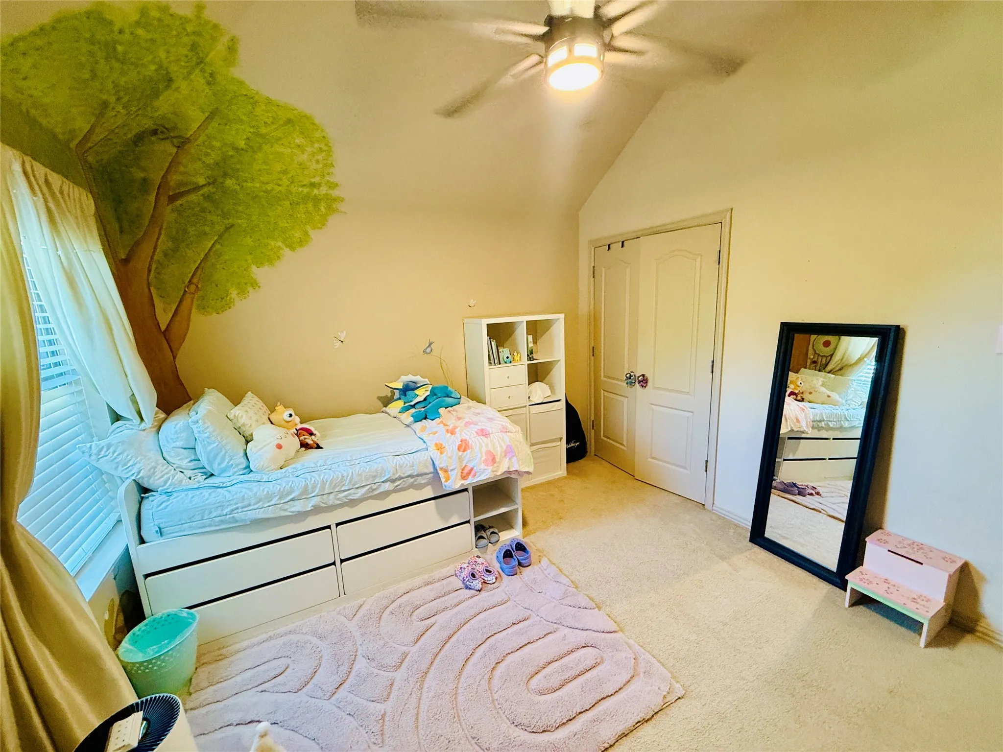 Vaulted ceiling room featuring a decorative tree mural, light-toned wall paint, and carpeting