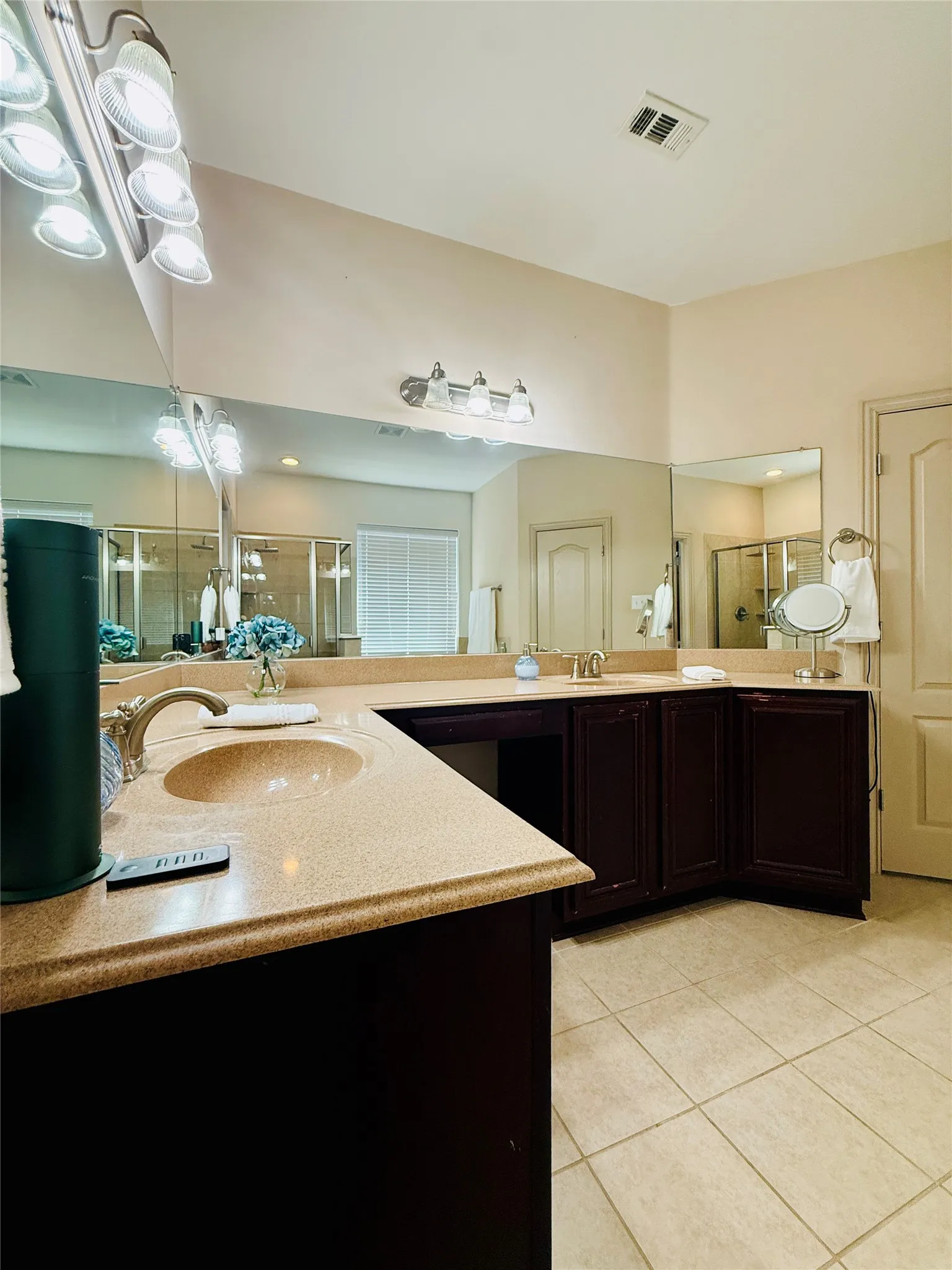 Bathroom vanity featuring a light-toned countertop with integrated sinks, dark wood-finish cabinetry, and an expansive wall-mounted mirror