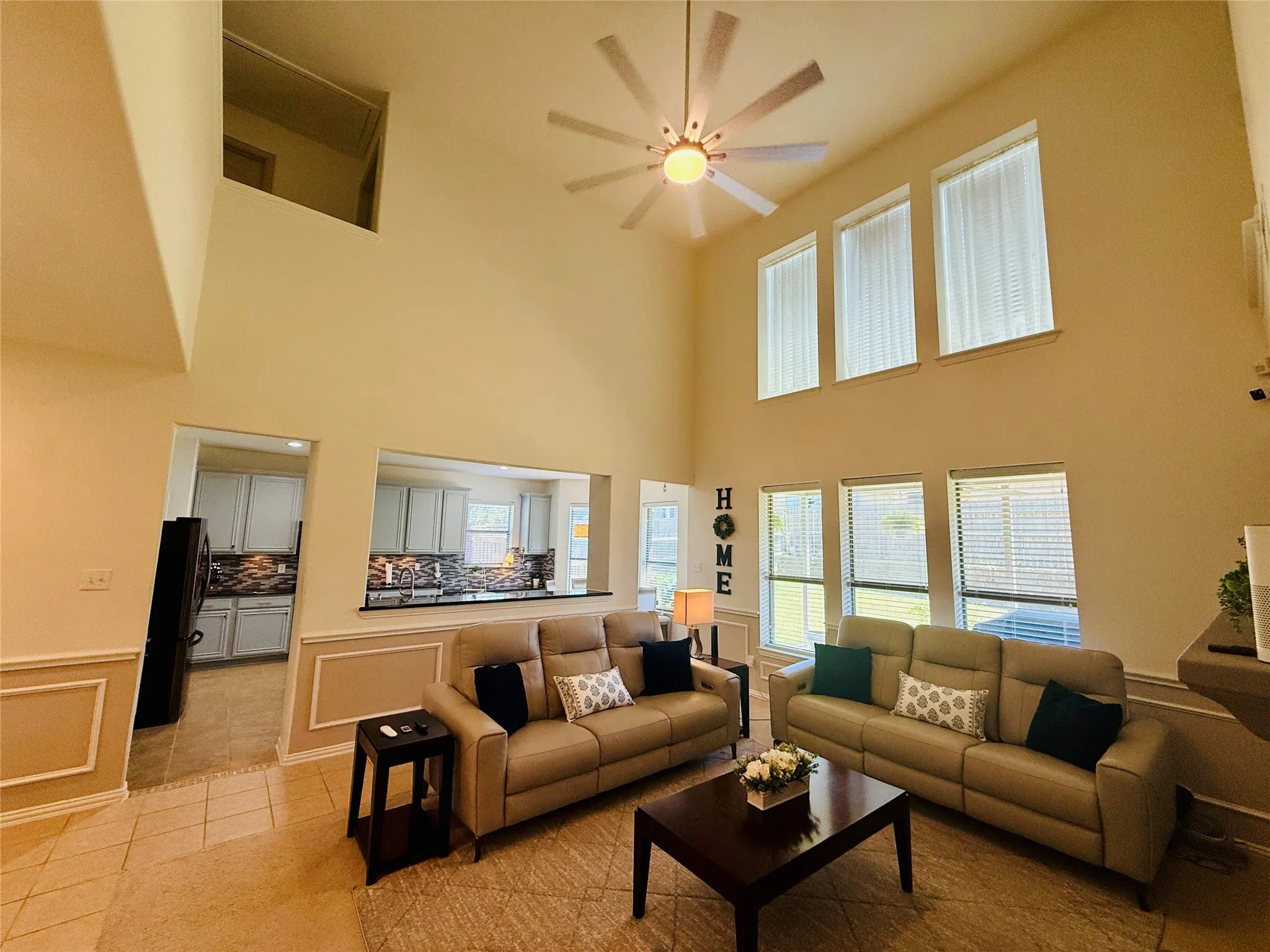 Spacious living area featuring high ceilings, a contemporary ceiling fan, and multiple windows with blinds