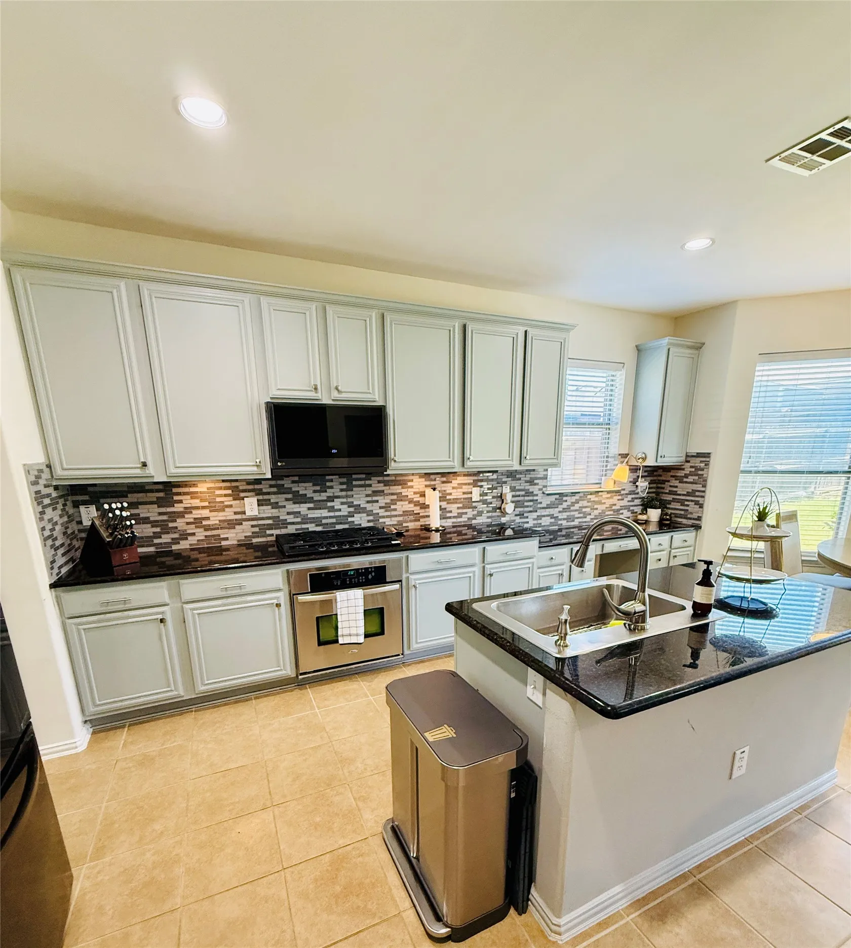 Kitchen featuring light-toned cabinetry, dark countertops, and a mosaic tile backsplash