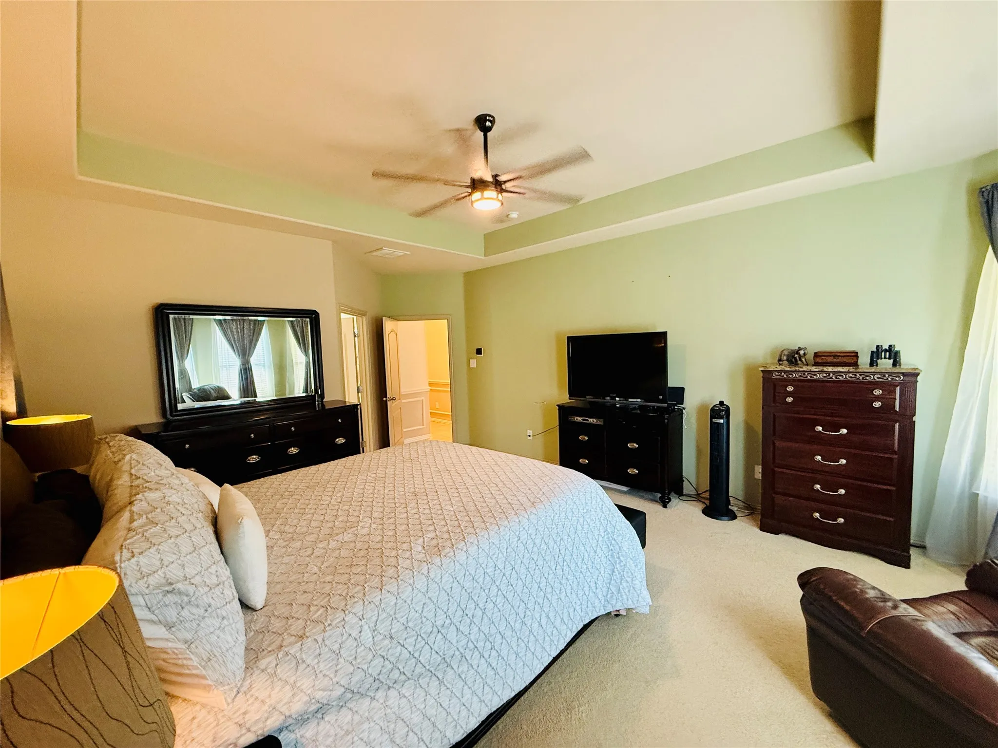 Carpeted sleeping area with tray ceiling and ceiling fan