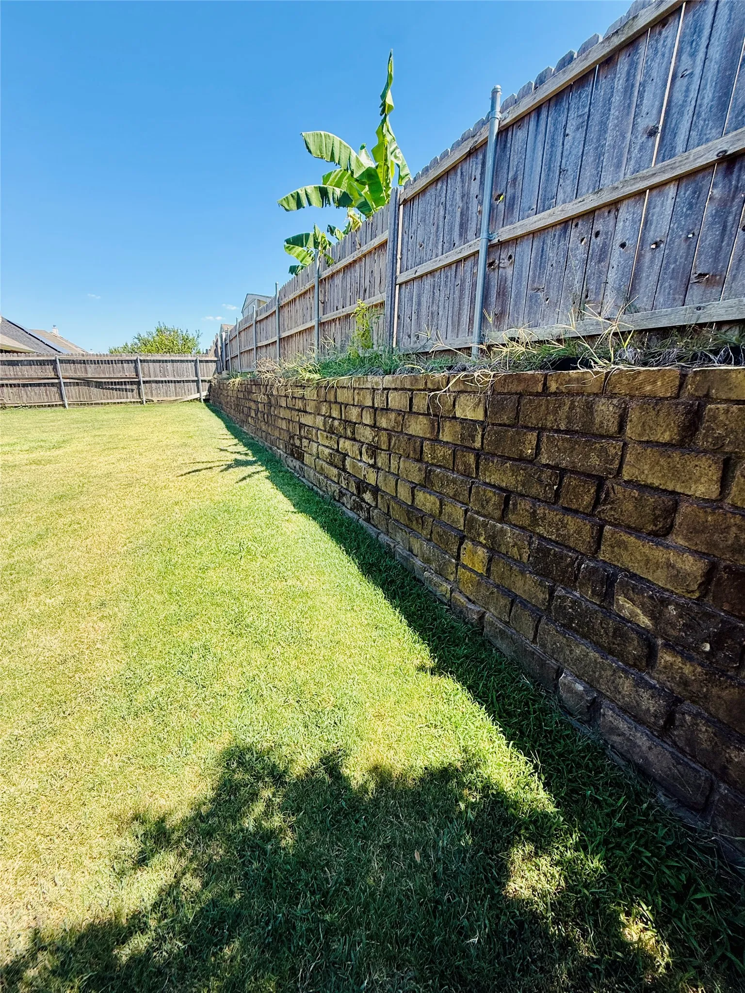 Expansive backyard featuring a stone retaining wall and a wood privacy fence