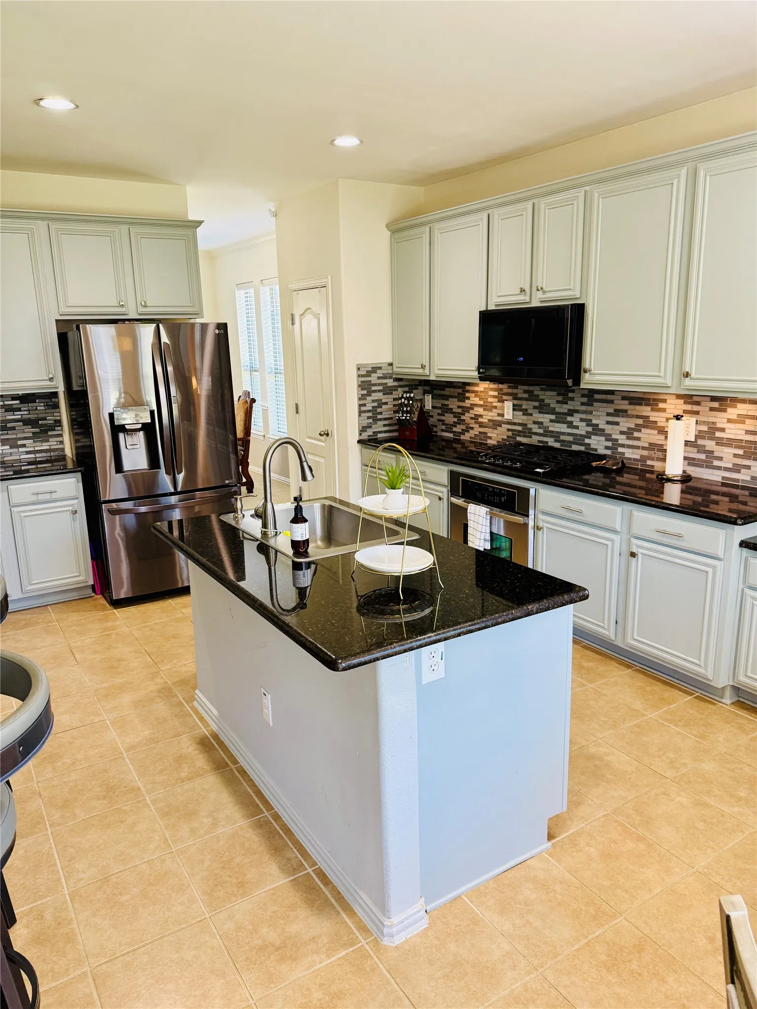 Kitchen with light-toned cabinetry, a spacious central island, and black speckled countertops