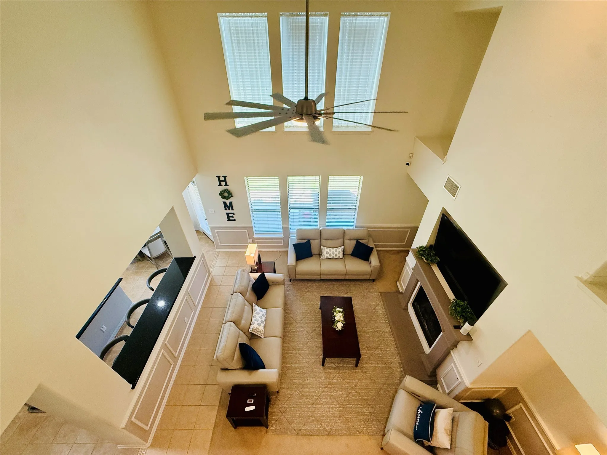 Spacious living area featuring high ceilings, a contemporary ceiling fan, and multiple windows with blinds