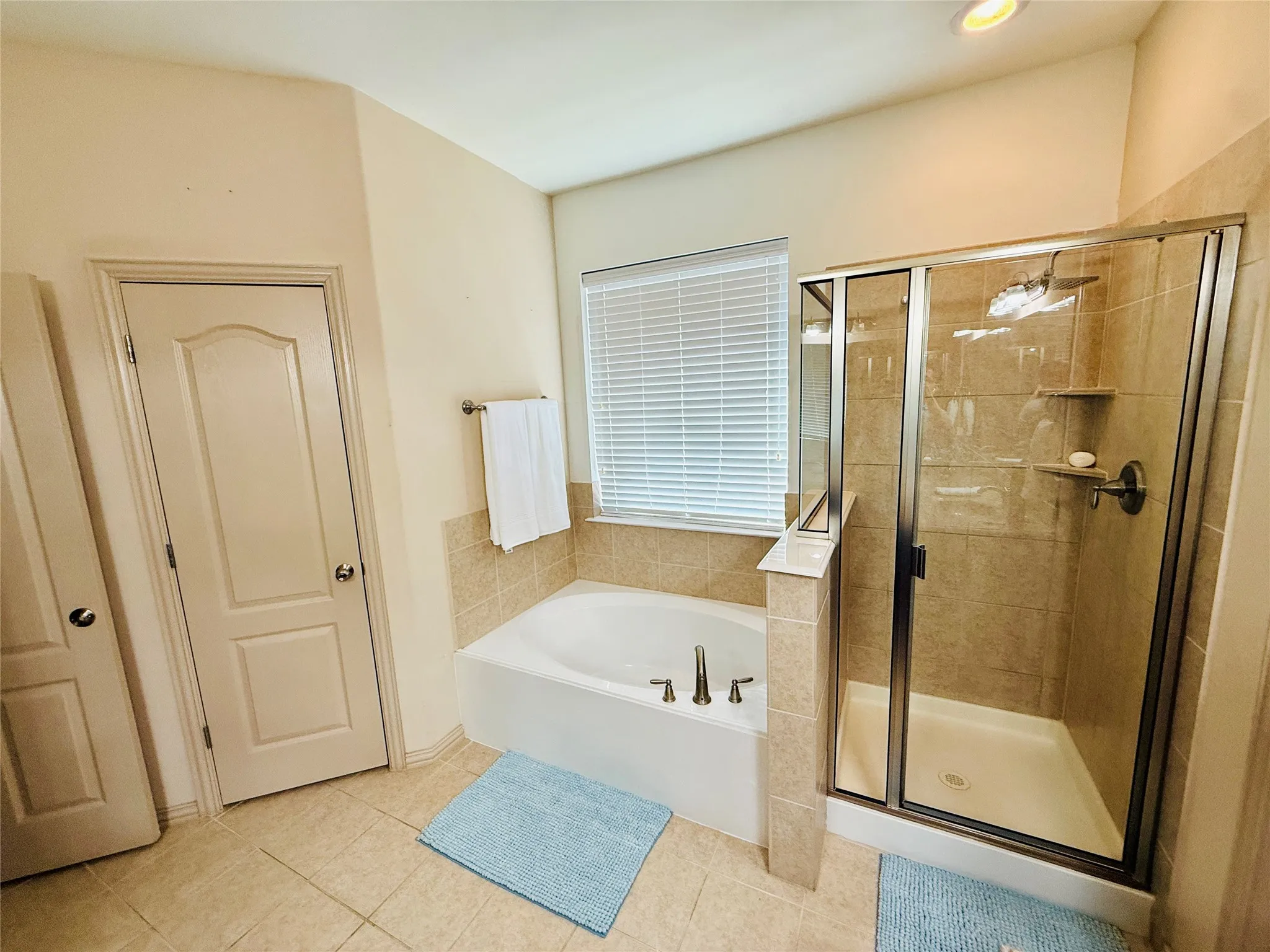 Bathroom featuring a built-in tub with deck-mounted fixtures, a glass-enclosed shower with tile surround, and neutral tile flooring