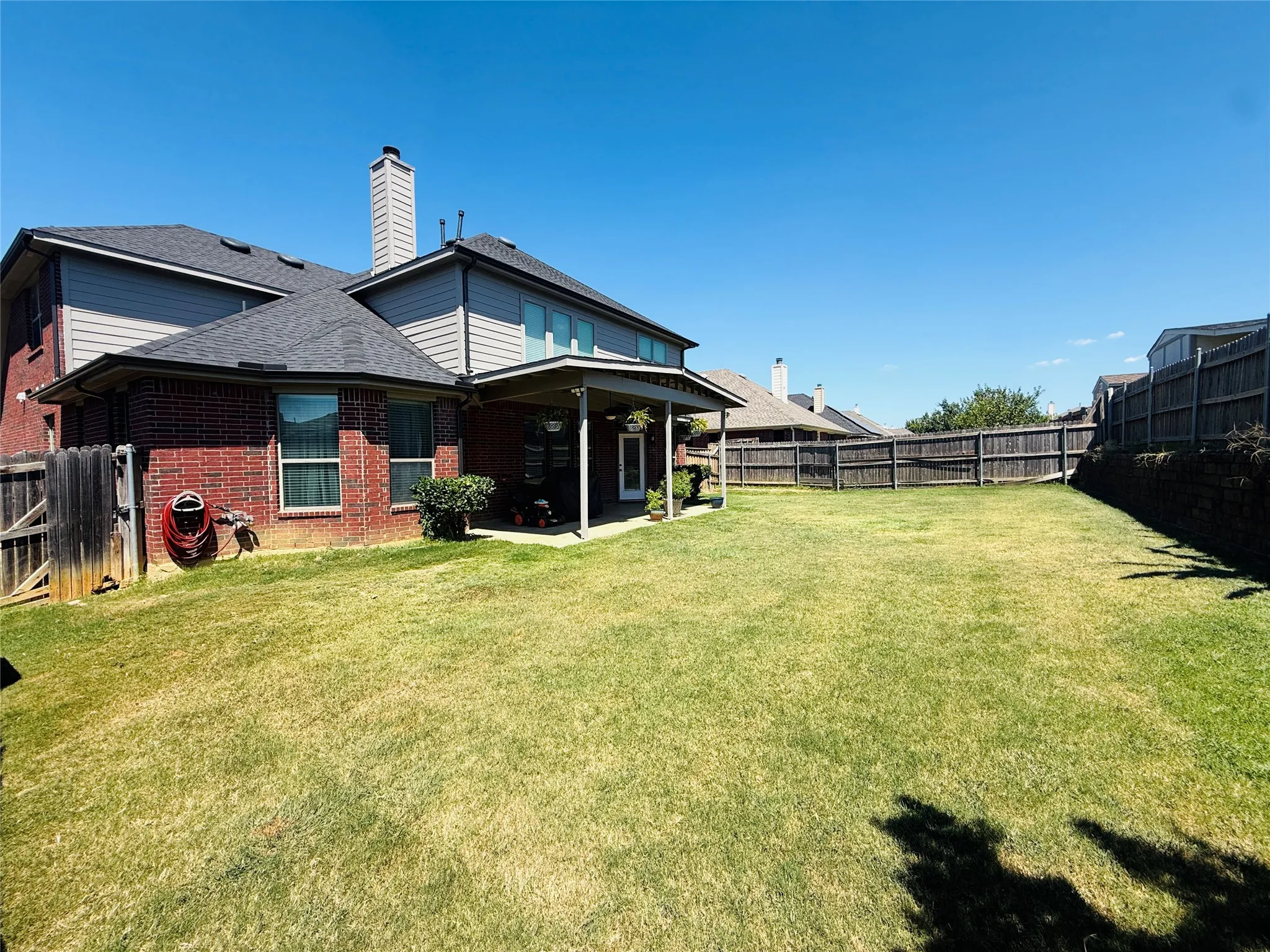 Expansive backyard featuring a covered patio, extensive lawn, full privacy fencing, and brick and siding exterior