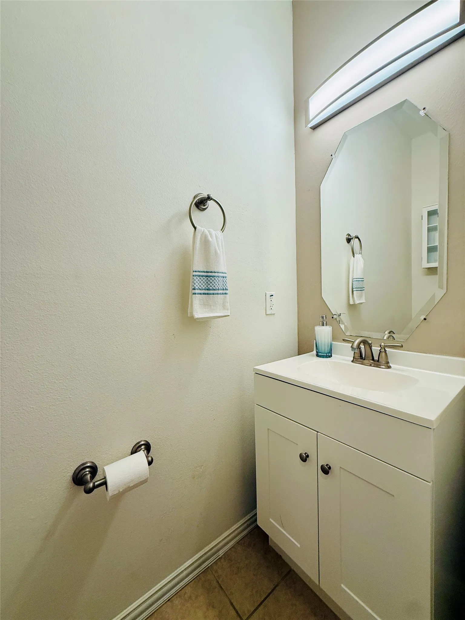 Bathroom featuring a white vanity with integrated sink, a beveled octagonal mirror, and a wall-mounted light fixture