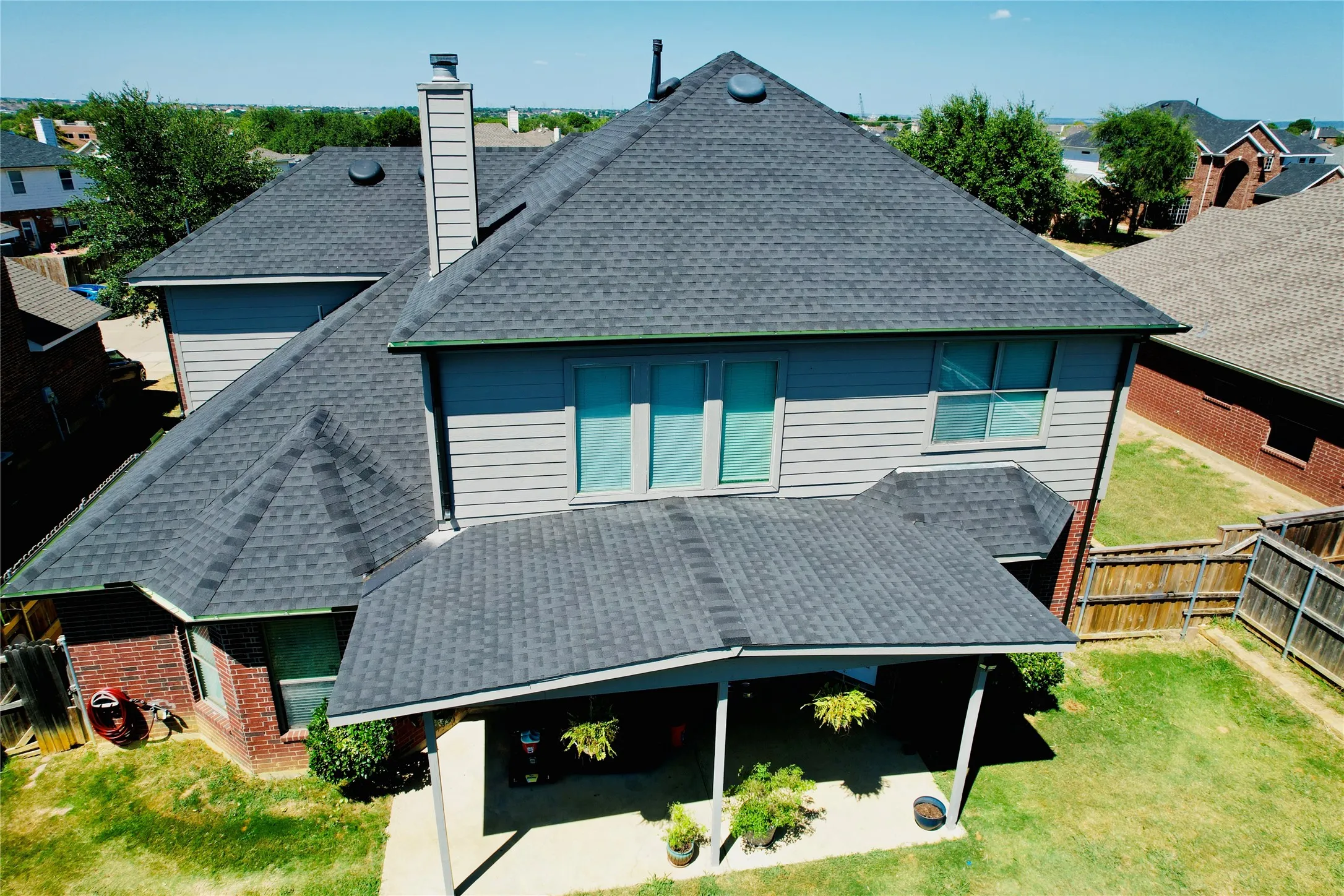 Expansive asphalt shingle roof system featuring multiple pitches and a covered patio area