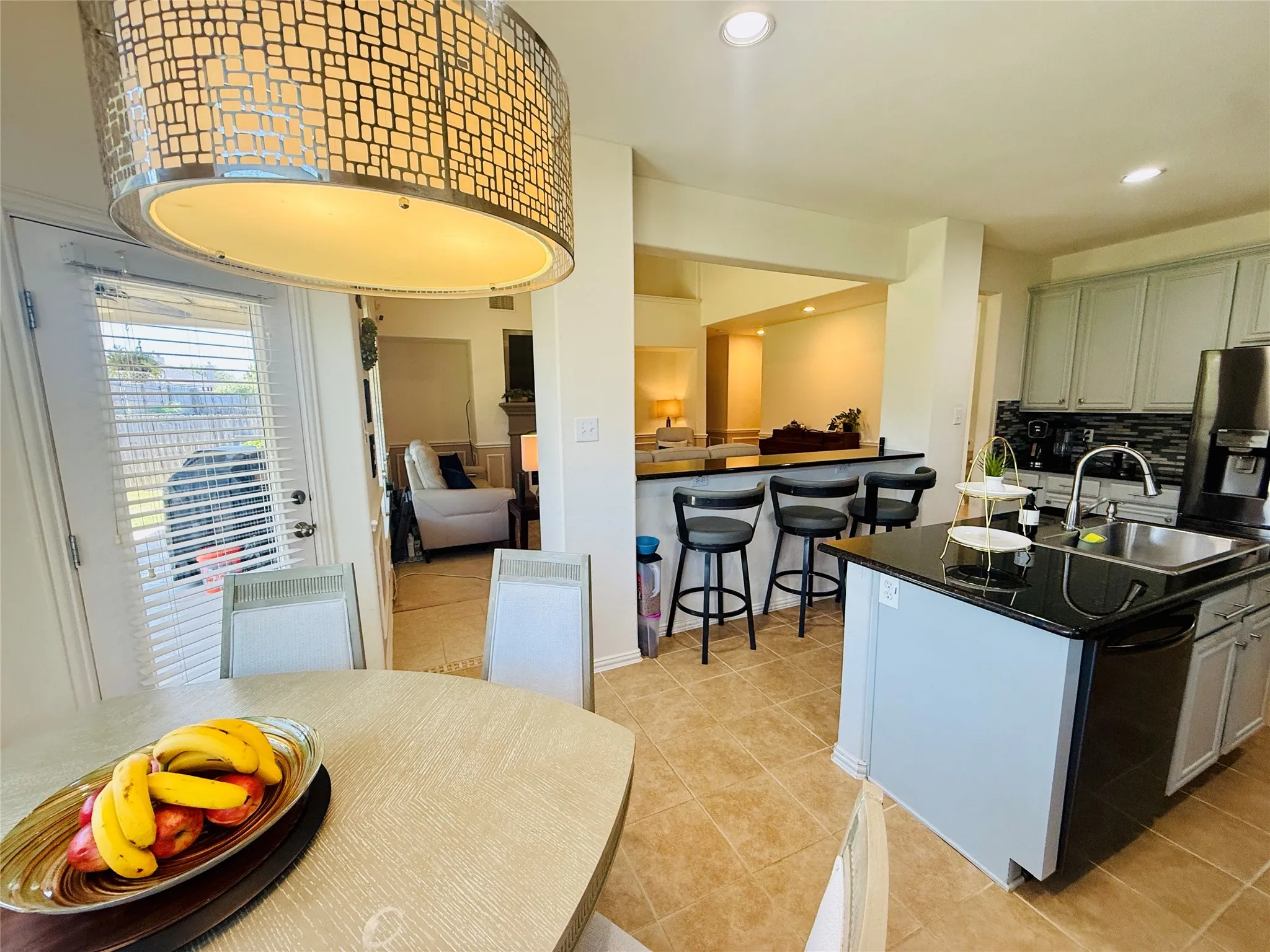 Kitchen featuring an island with a stainless steel sink, black countertops, light gray cabinetry, and tile flooring