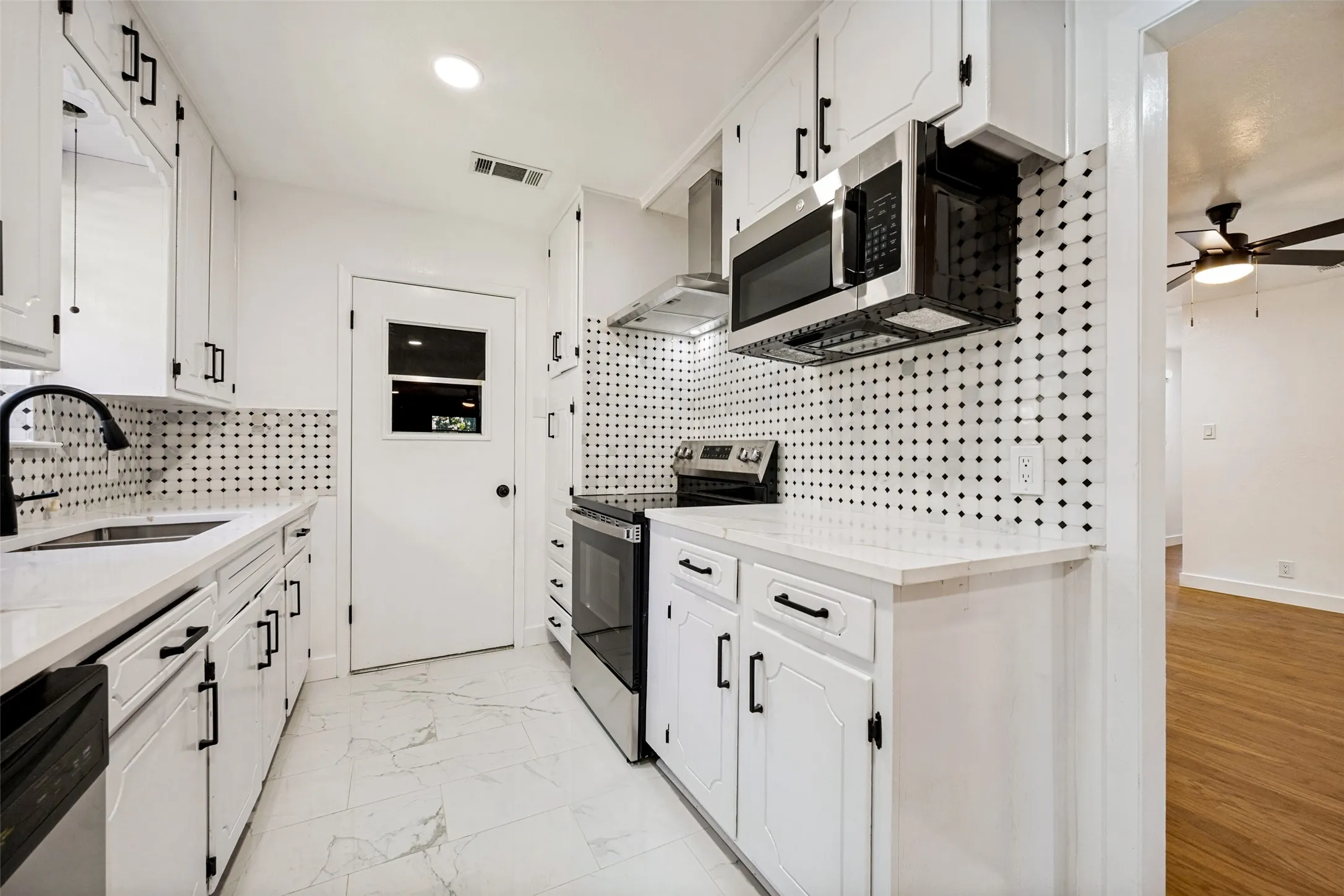 Galley kitchen featuring white cabinetry, quartz countertops, stainless steel appliances, a unique black and white patterned backsplash, and white tile flooring