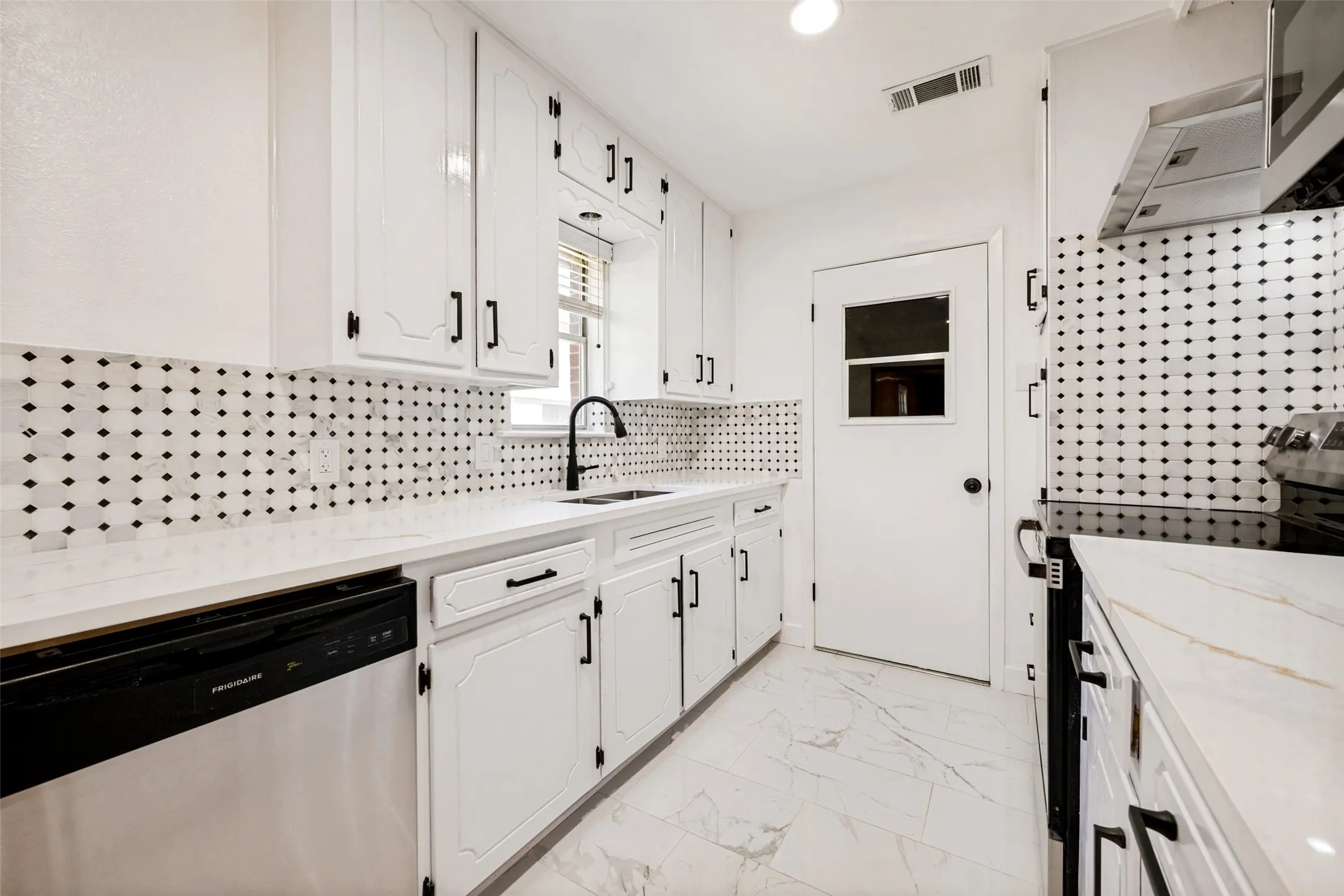 Bright kitchen featuring white cabinetry, black hardware, black and white geometric backsplash, white countertops, and stainless steel appliances