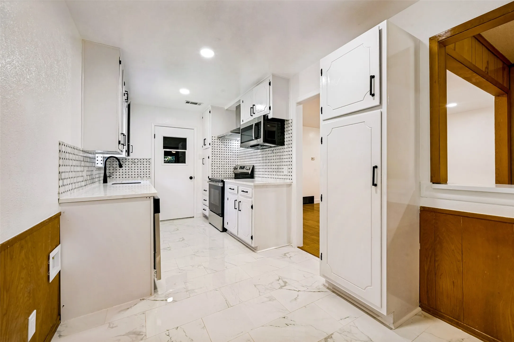 Kitchen featuring white cabinetry, stainless steel appliances, a patterned tile backsplash, and light-toned marble-look flooring