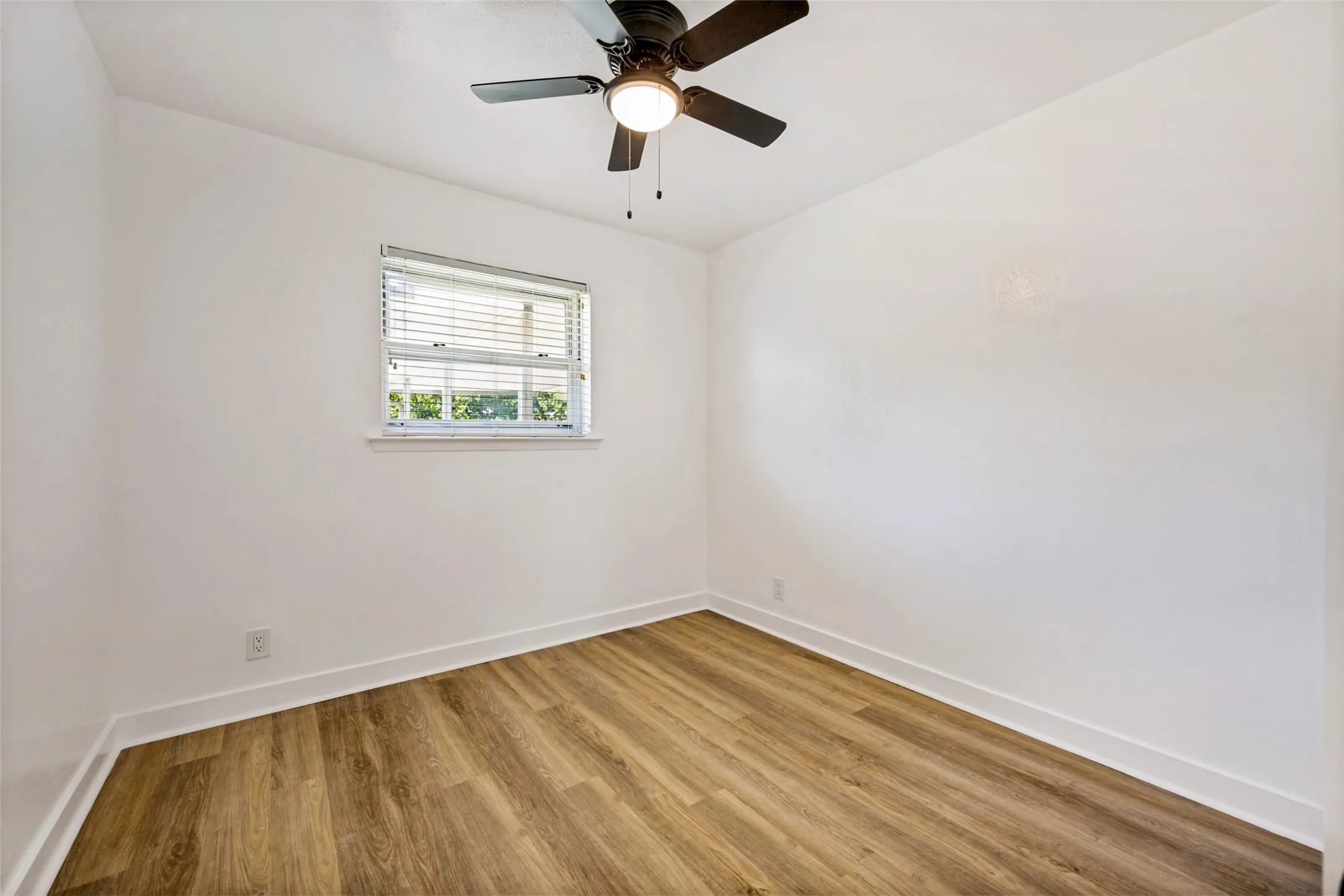 Bright room featuring a window with blinds, a ceiling fan with integrated lighting, wood-finish flooring, and white baseboards