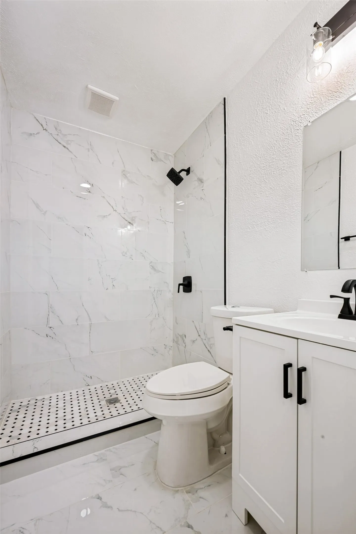 Modern bathroom featuring a walk-in shower with white and gray veined tile surround, black and white mosaic shower pan, and matte black fixtures