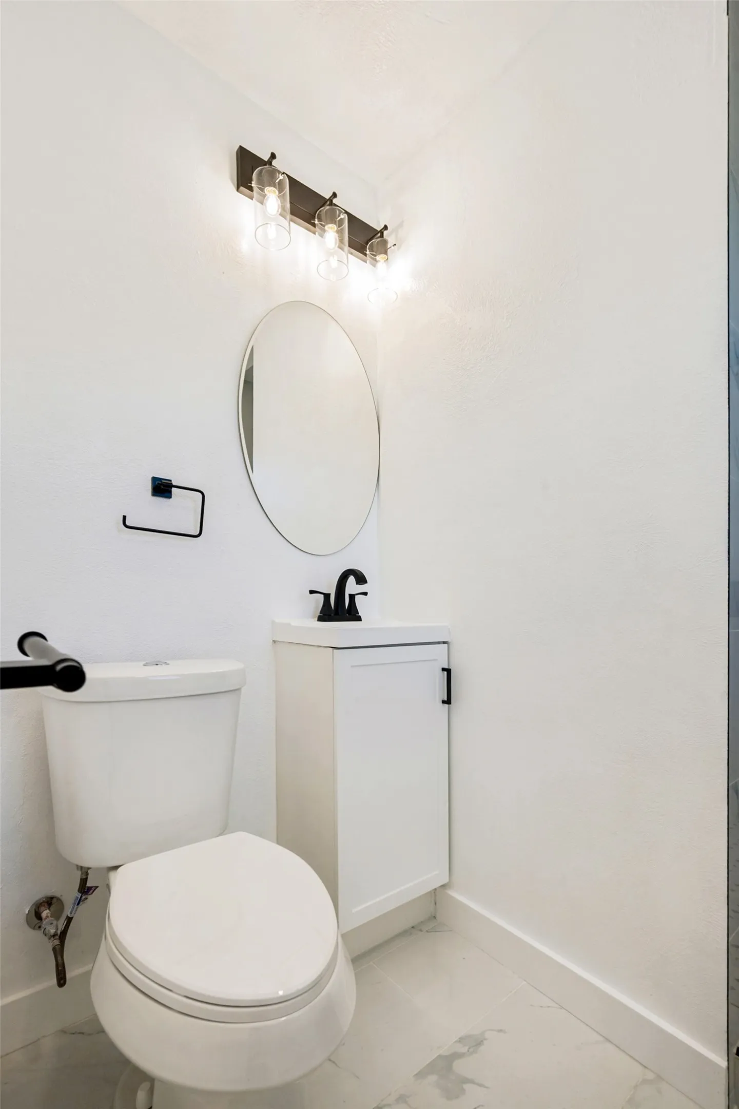 Compact bathroom featuring a white vanity cabinet, matte black faucet, and oval mirror