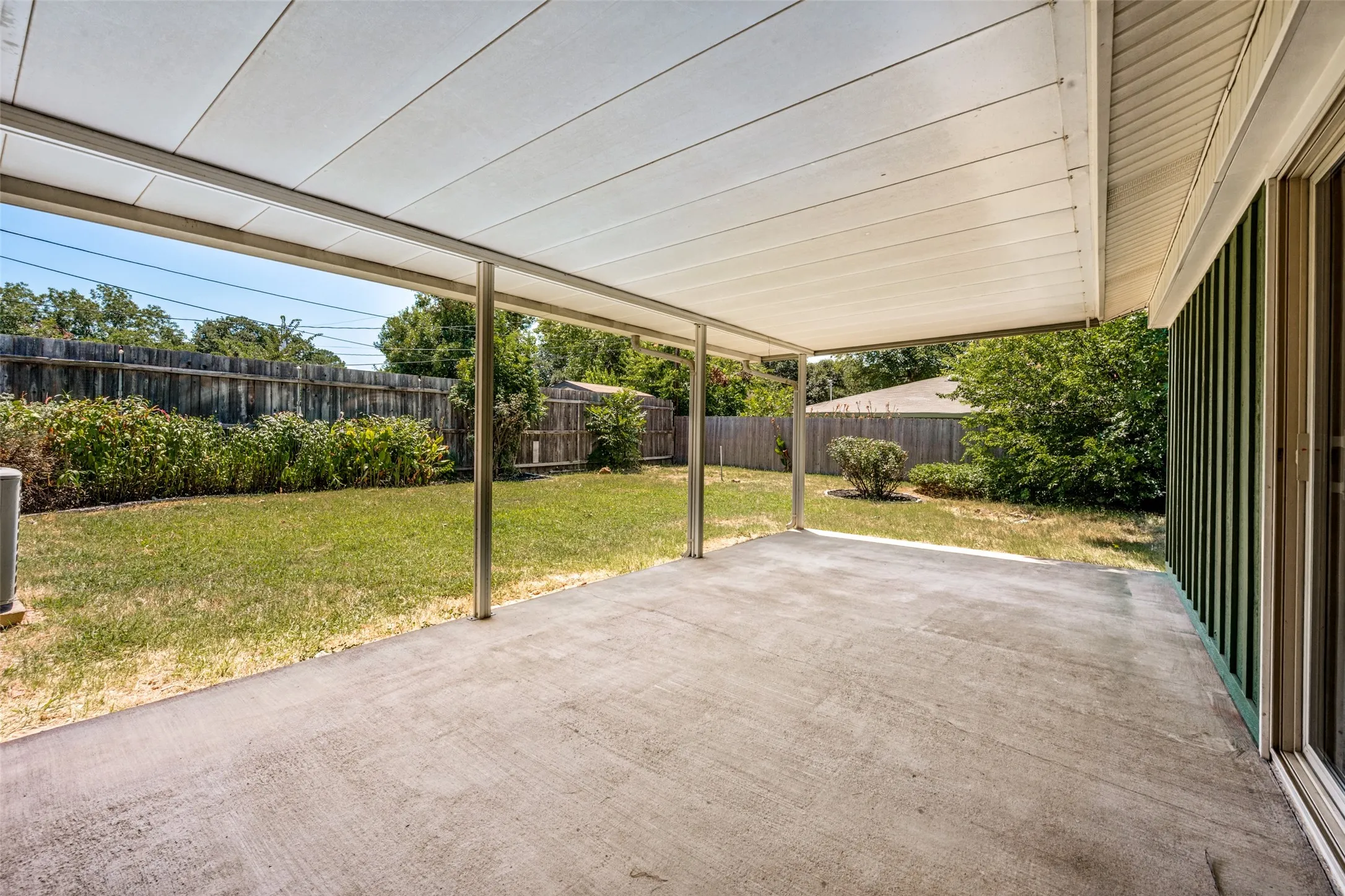 Expansive covered patio featuring a concrete surface, supported by metal posts, and an overhead panel roof
