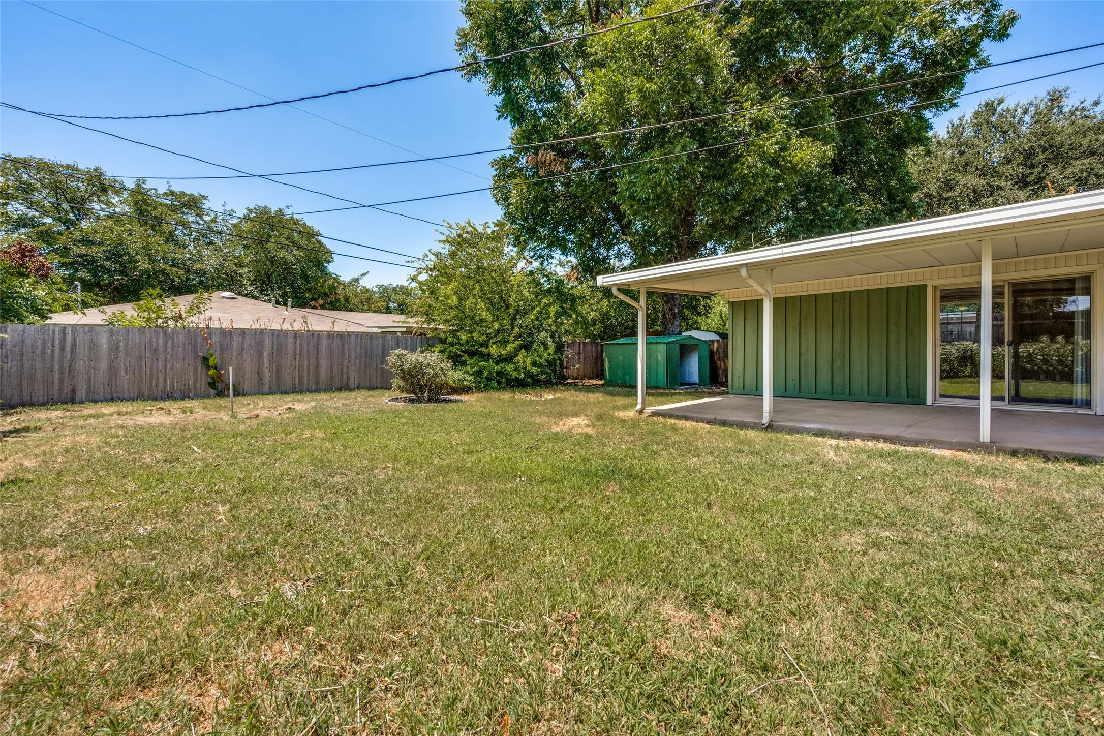 Spacious backyard featuring a covered concrete patio, wood privacy fencing, and mature trees