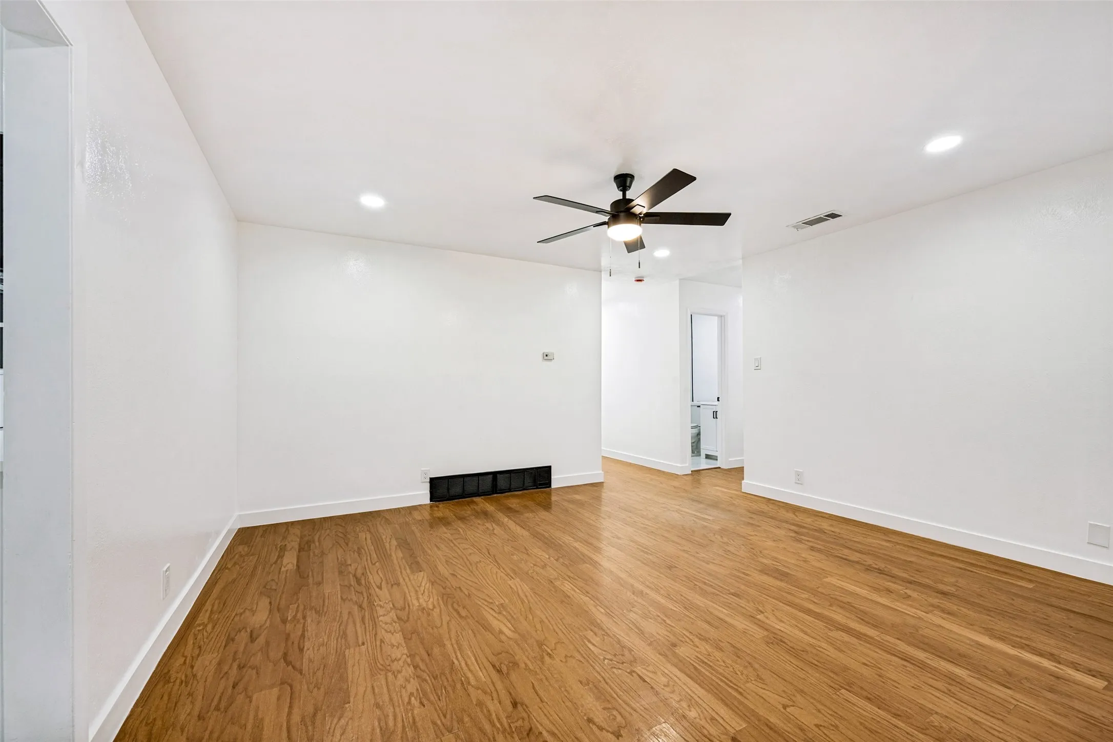 Spacious room featuring wood-finish flooring, recessed ceiling lights, a ceiling fan with integrated lighting, and white baseboards
