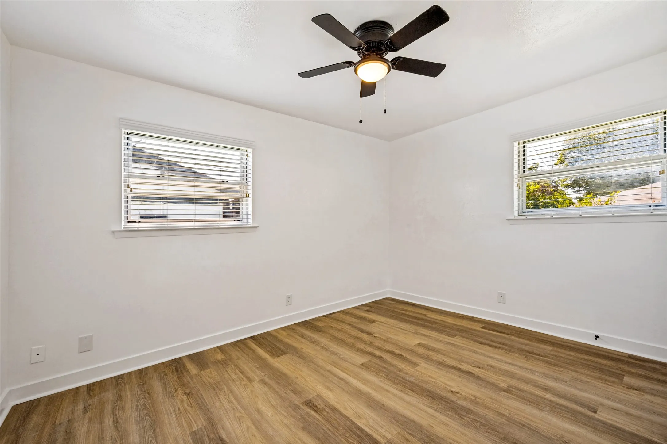 Interior room featuring bright white walls, wood-finish flooring, and white baseboards