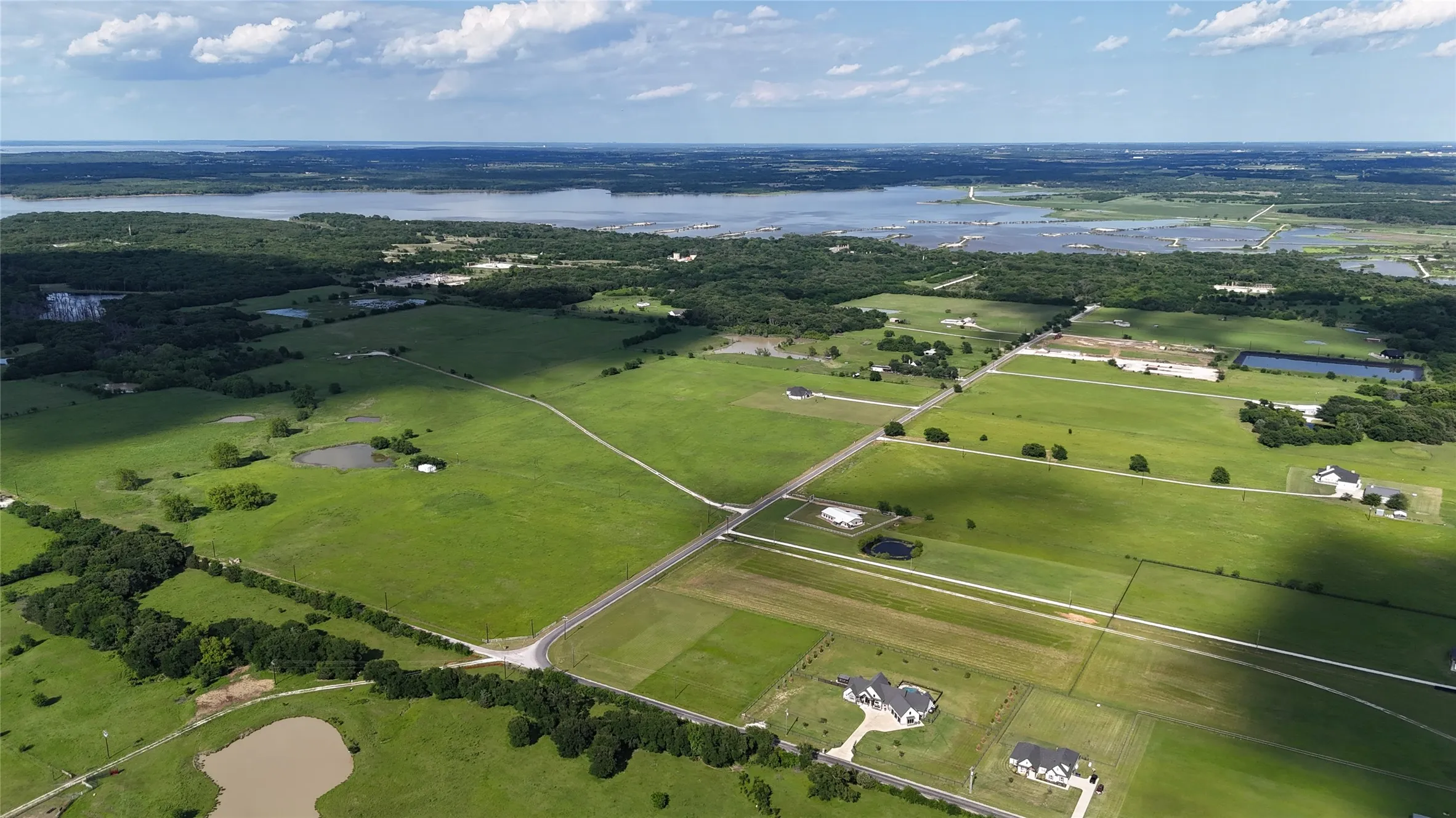 Expansive aerial landscape featuring extensive green fields, mature trees, and multiple bodies of water